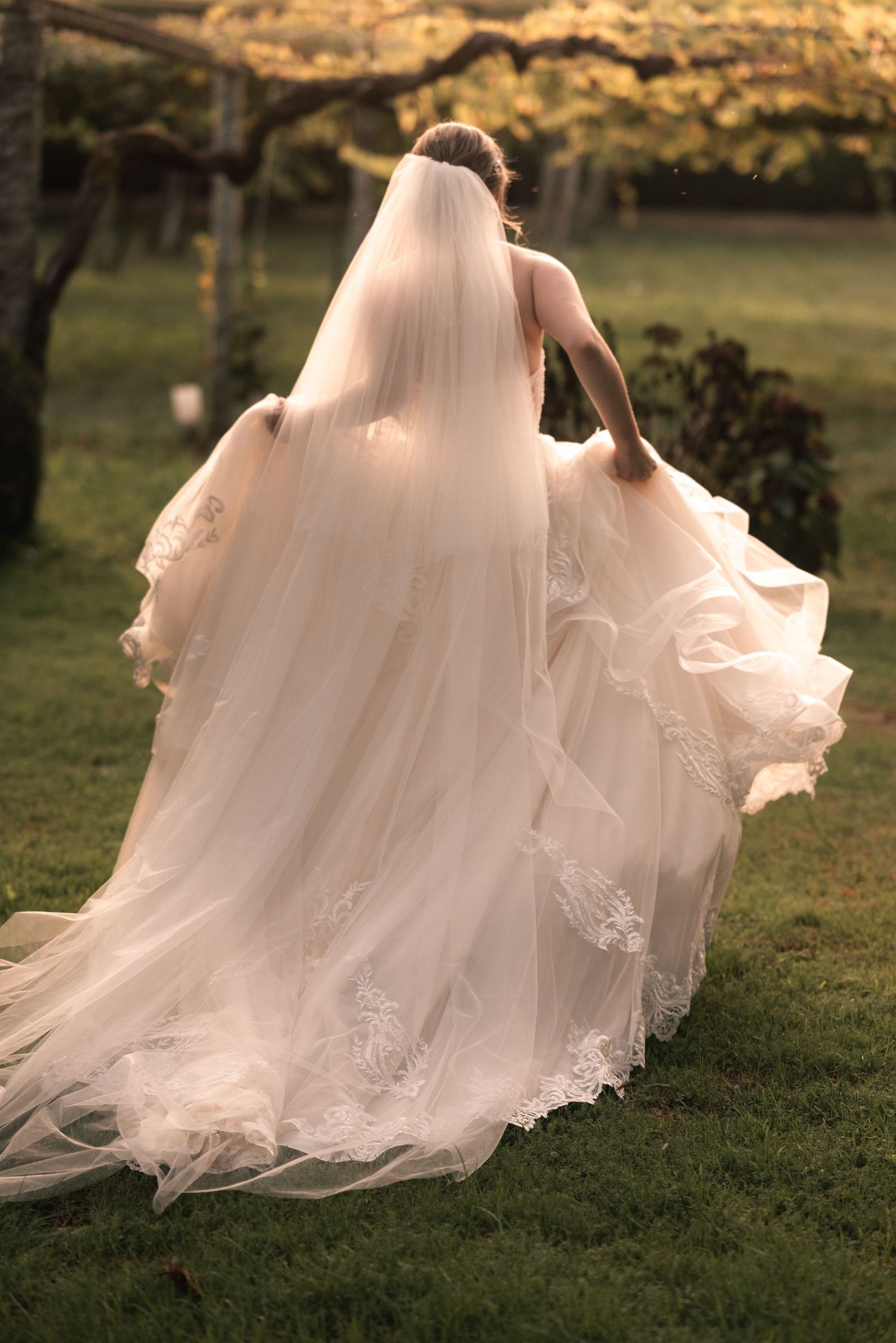A flowing white wedding dress train sweeps across green grass in a romantic outdoor setting at golden hour.