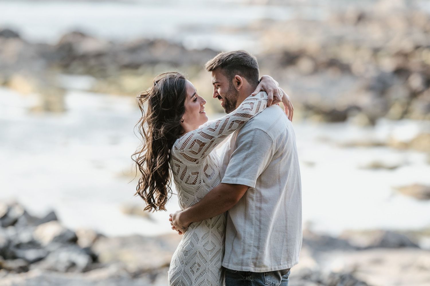 A romantic couple dances together on rocky coastal terrain at sunset creating a dreamy silhouette.
