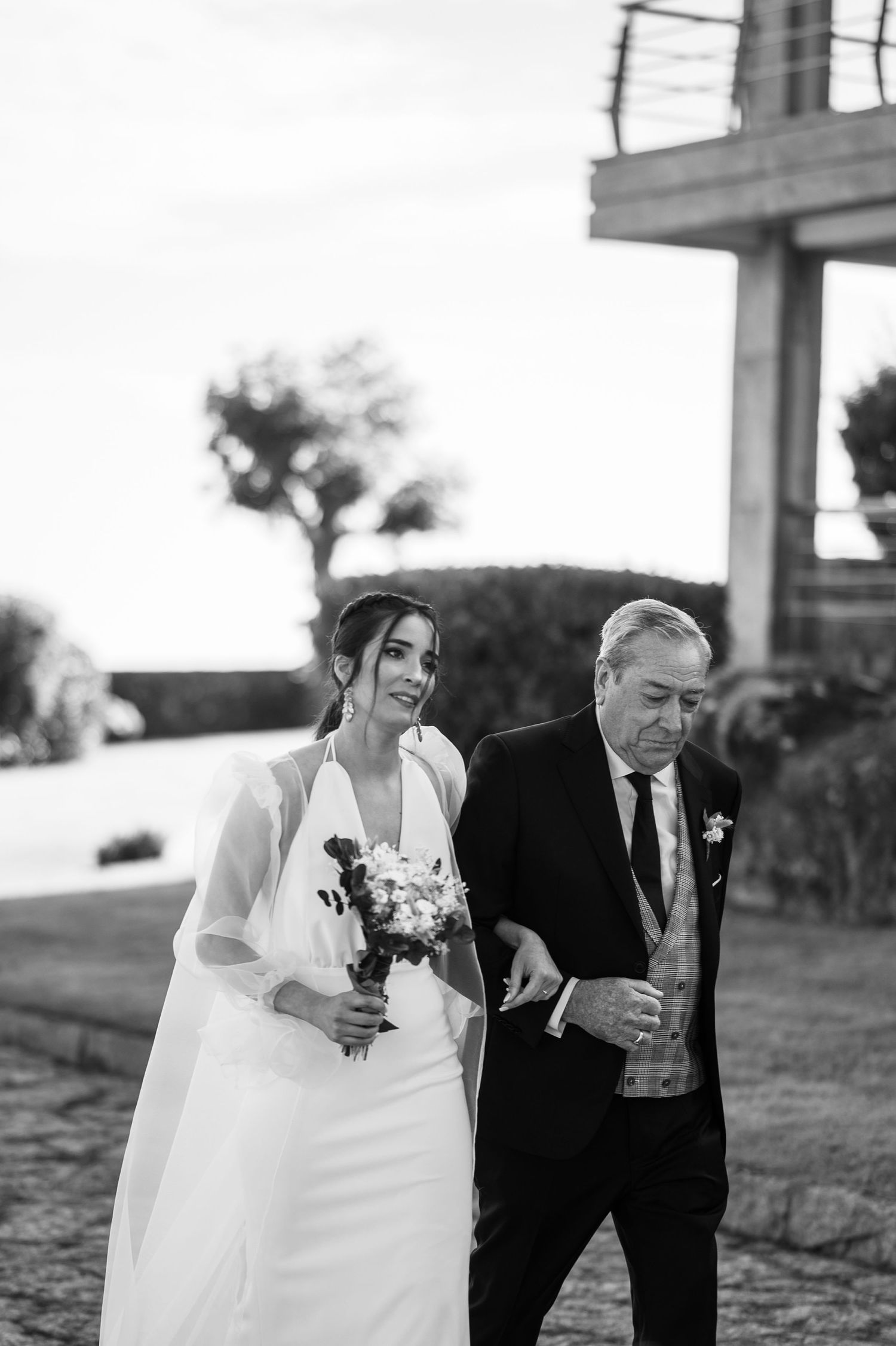 A wedding couple laughs together while walking on a scenic outdoor path at sunset.