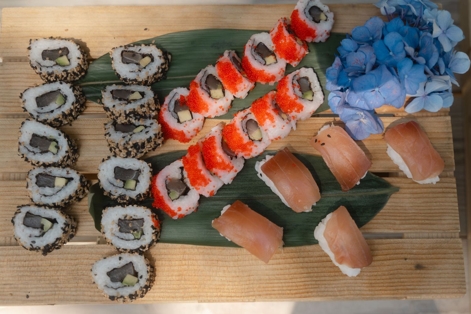 Colorful assortment of sushi rolls arranged on bamboo leaves against a wooden surface.