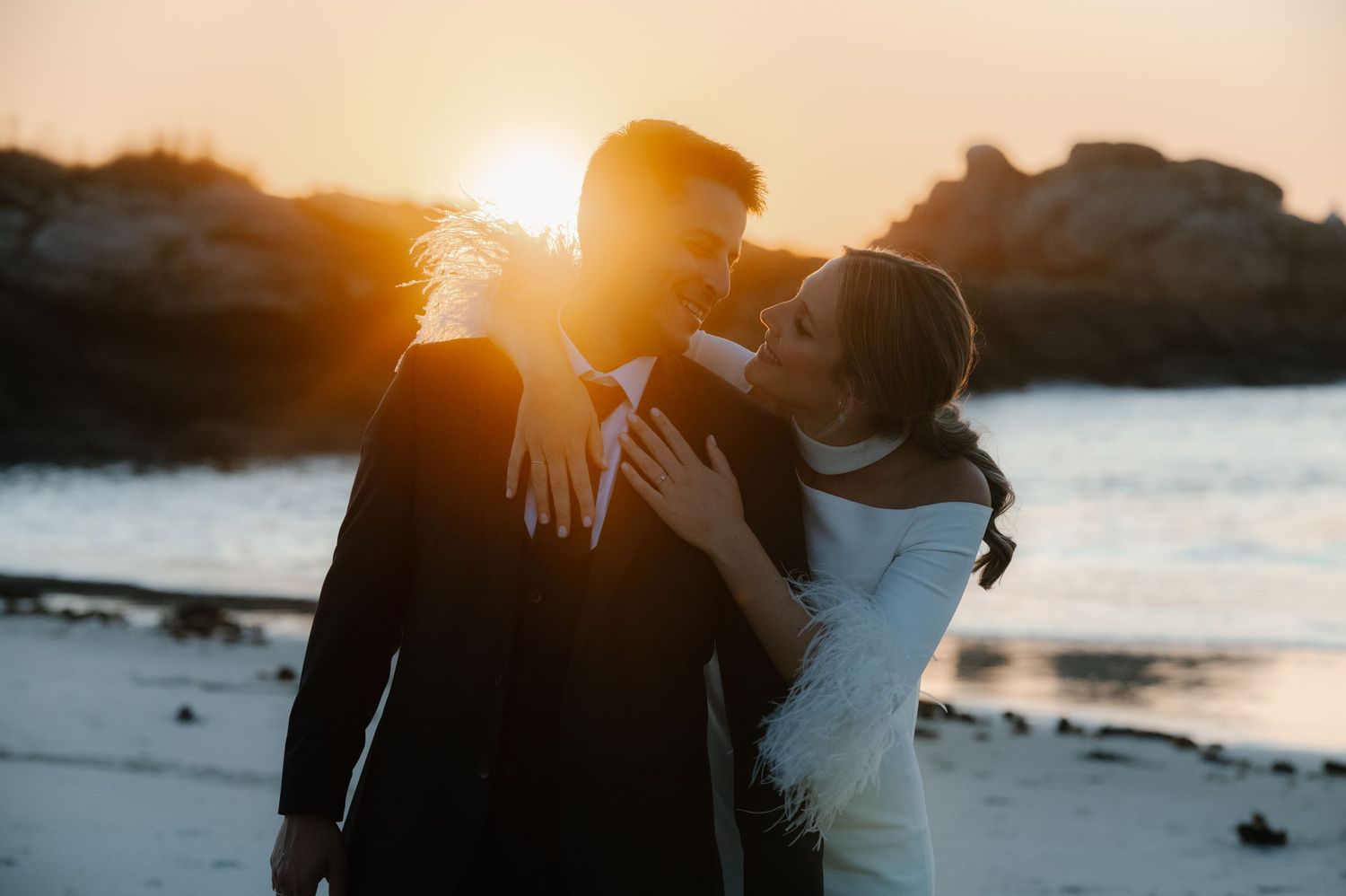 Romantic sunset silhouette of wedding couple embracing by the ocean.