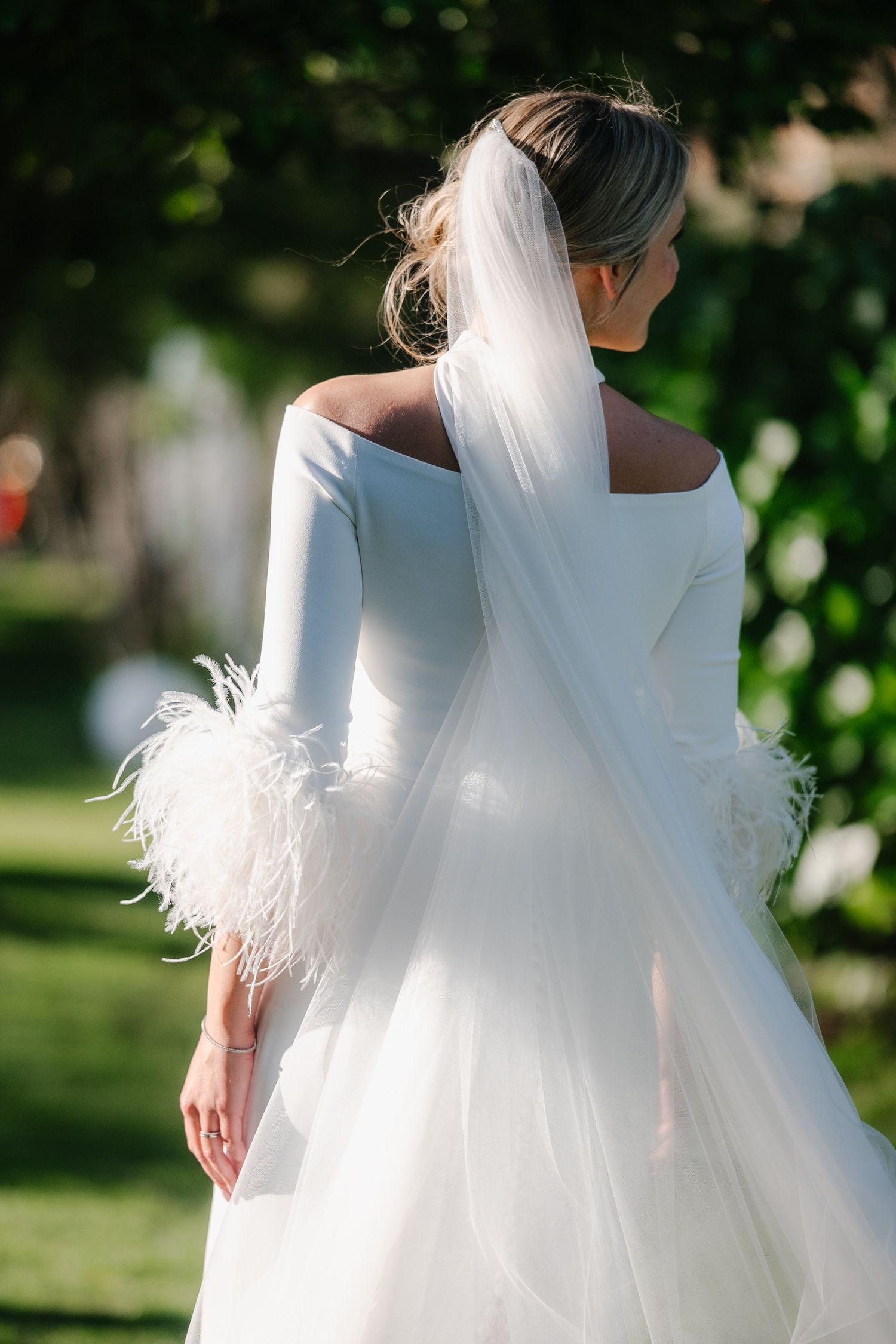 An elegant white wedding dress with feather details photographed in a garden setting.