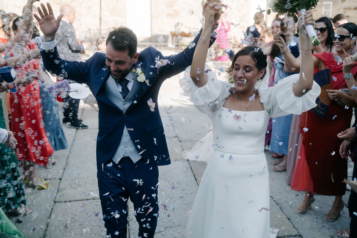 Wedding guests shower newlyweds with white confetti as they exit the church in a joyful celebration.