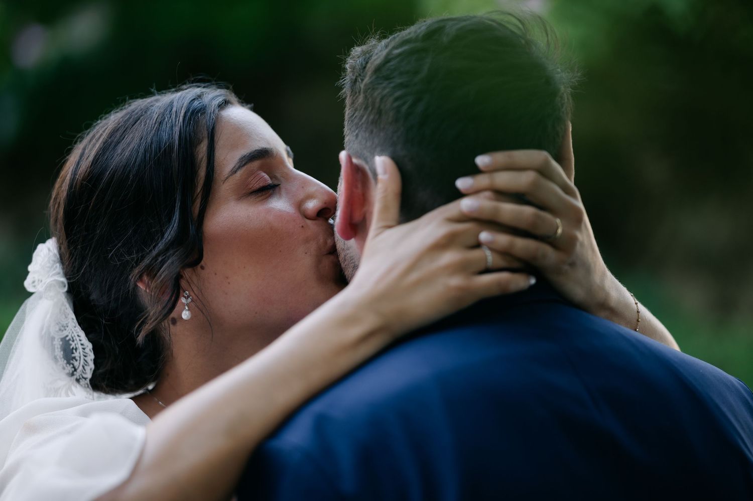 A couple in wedding attire embraces and kisses in a romantic outdoor setting.
