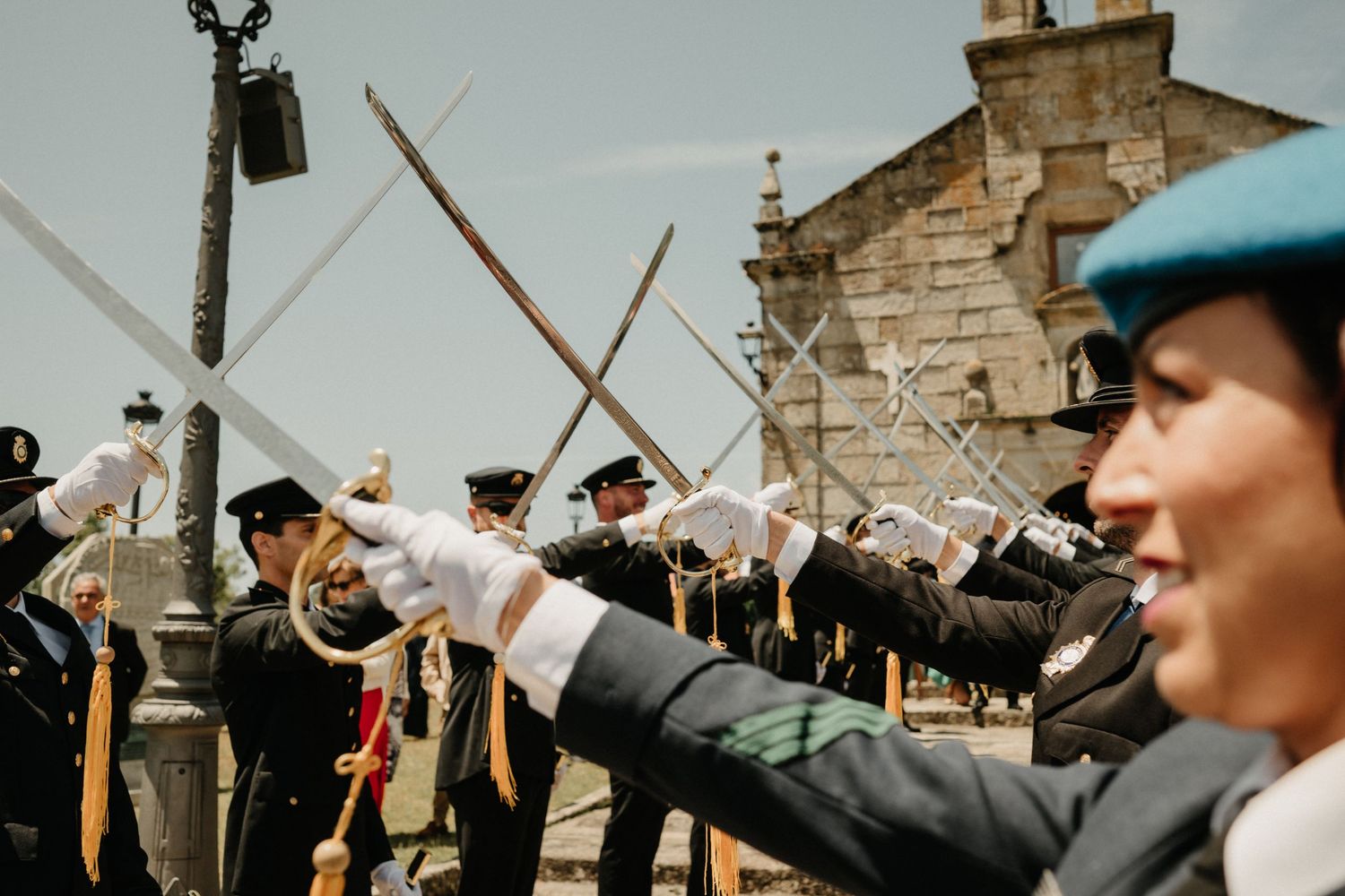 Military wedding ceremony takes place against historic stone fortress backdrop under blue skies.