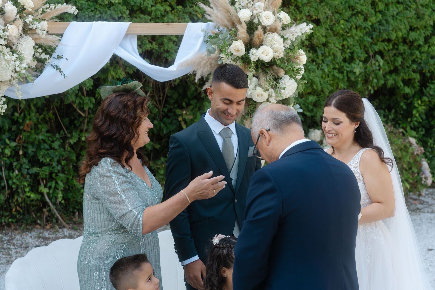 A series of intimate outdoor wedding moments with guests and couple surrounded by white floral arrangements and greenery.