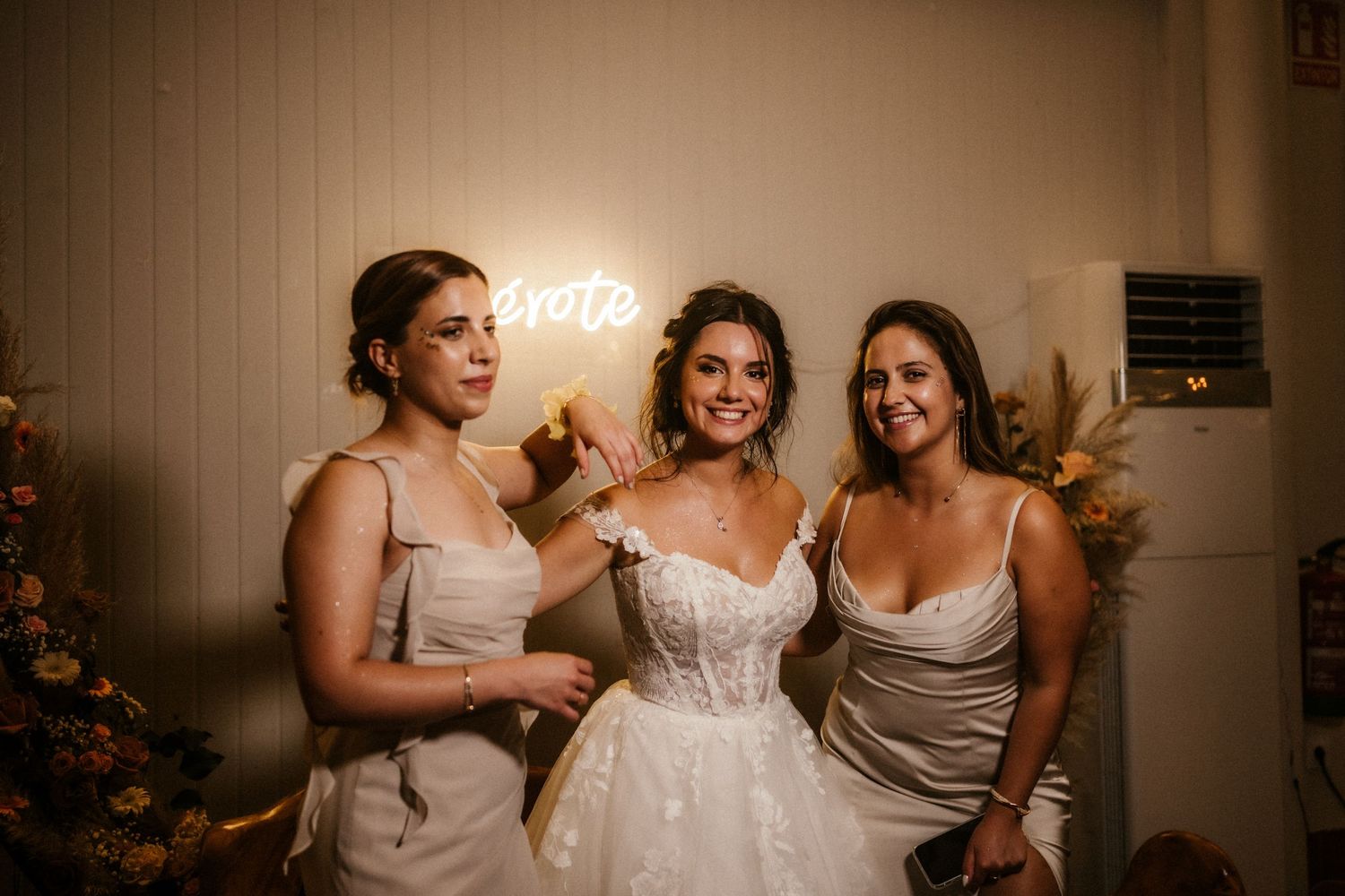 Three women in formal attire share a joyful moment together at a wedding celebration.