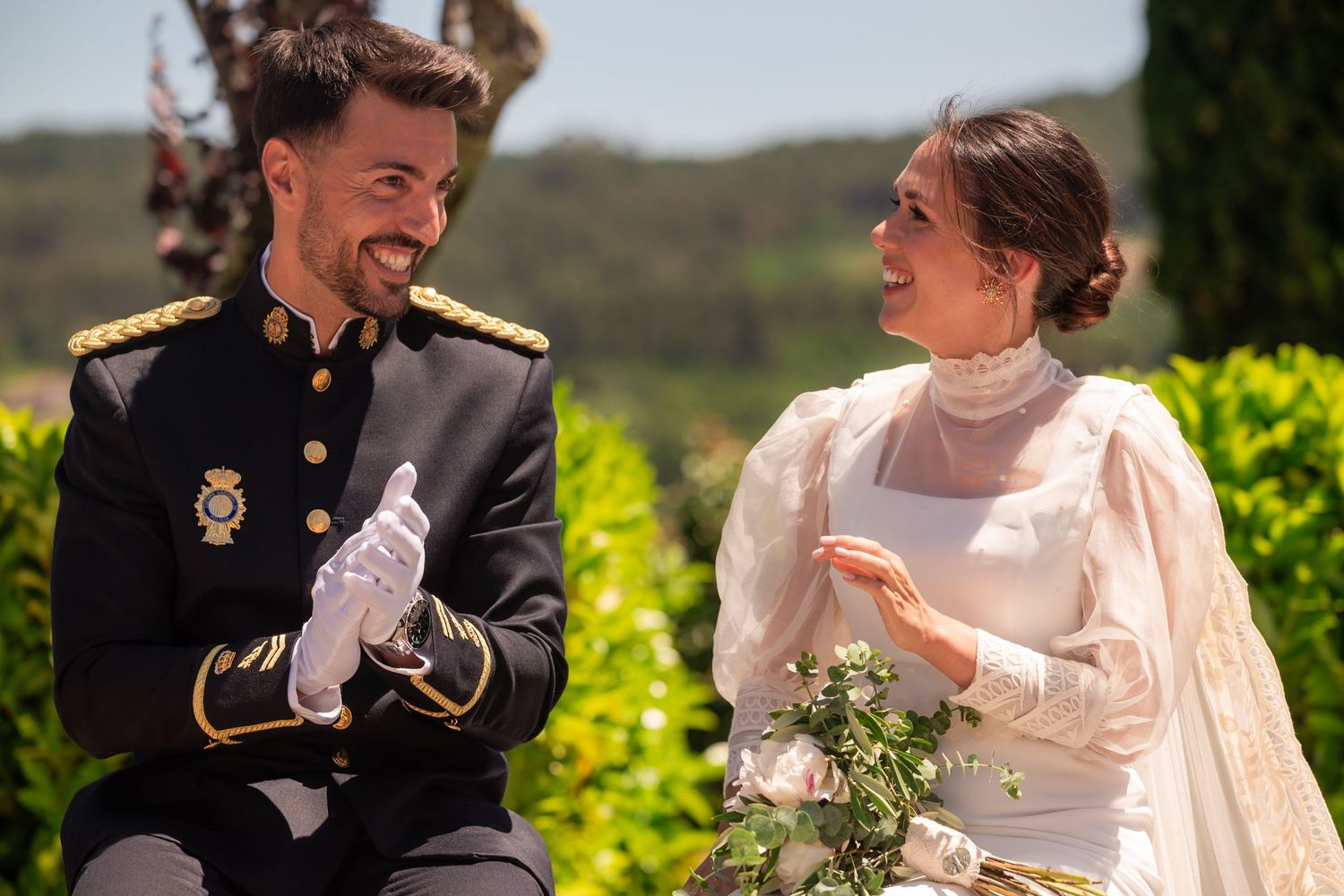 A joyful couple in wedding attire share a laugh together outdoors on their special day.