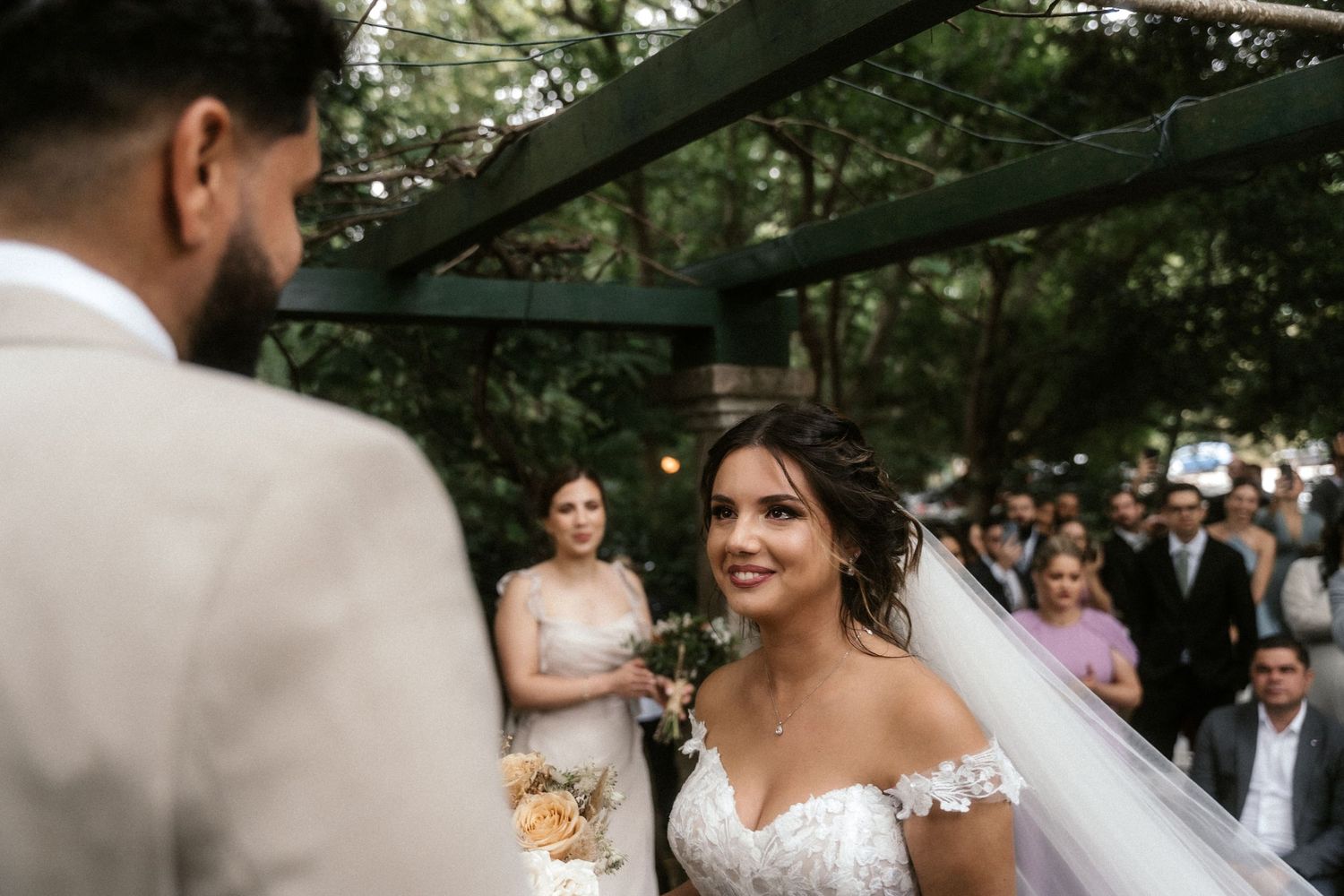 An intimate wedding ceremony moment captured outdoors with guests watching in the background.