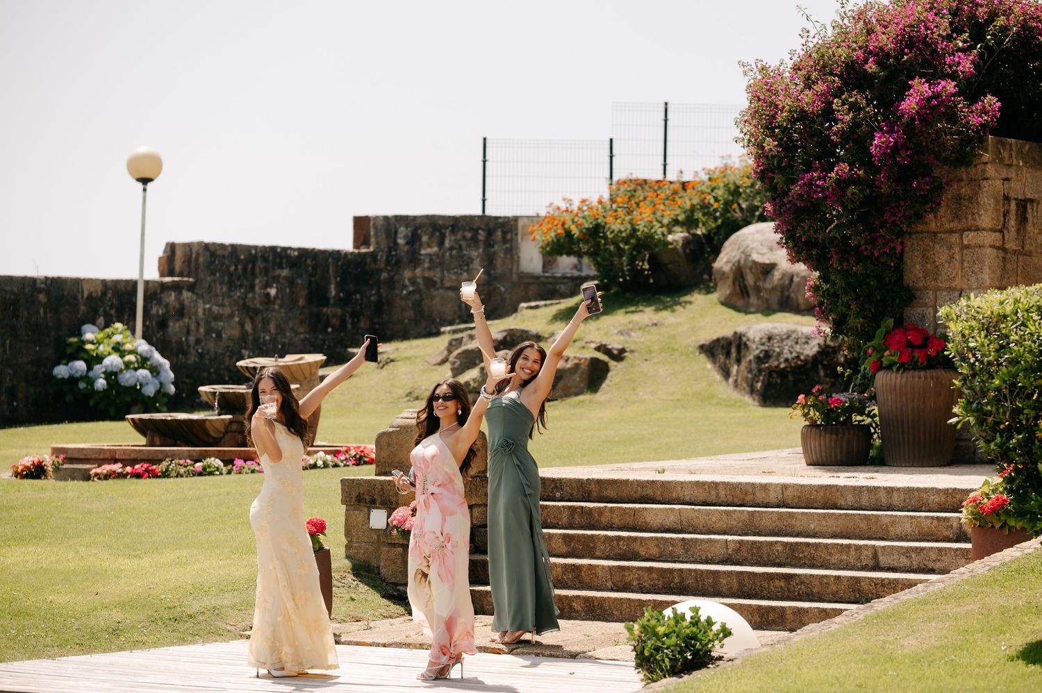 People enjoying a sunny day on landscaped garden steps with blooming flowers and stone walls at an outdoor venue.