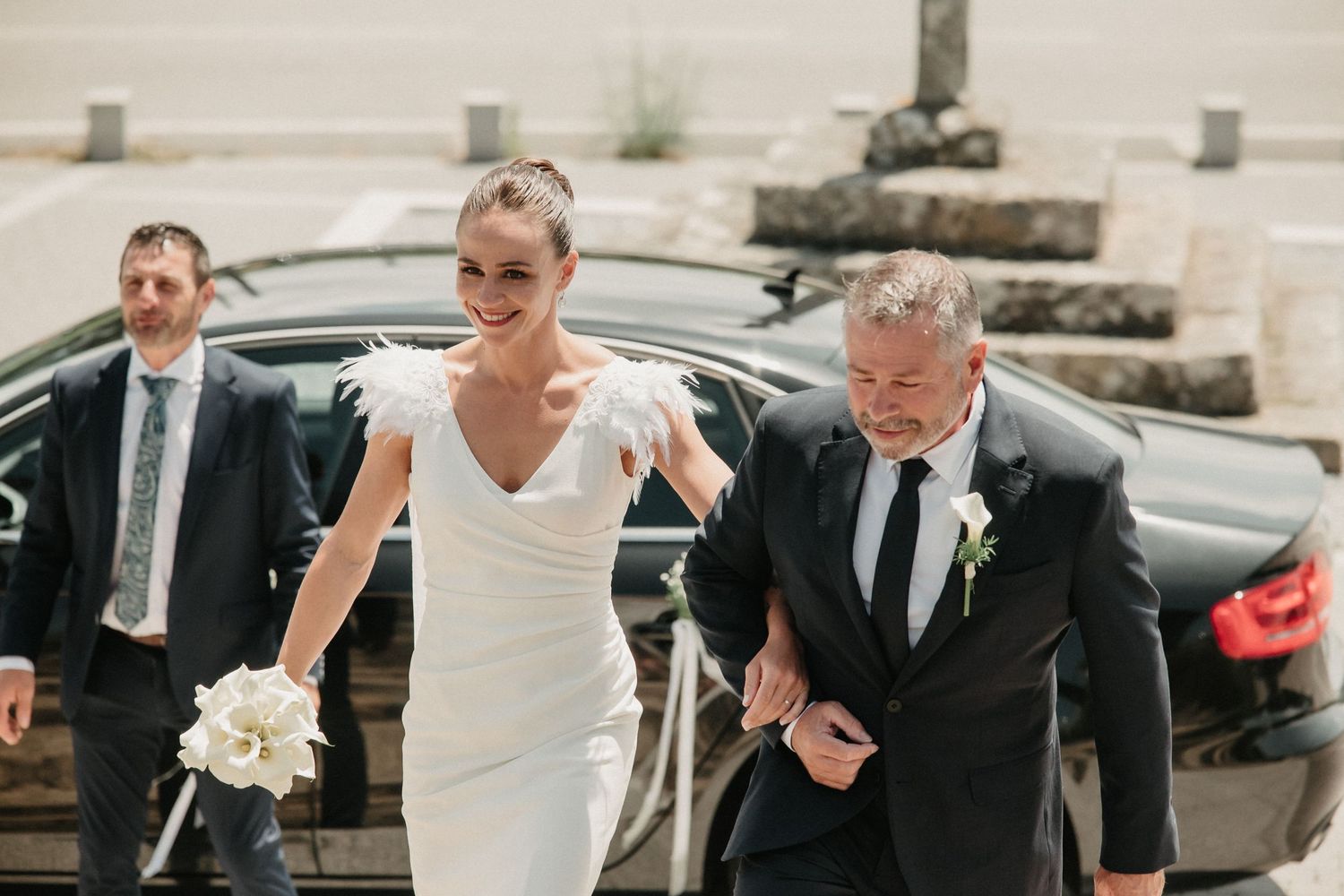 A couple in wedding attire walks together on a sunny day while holding hands and laughing.