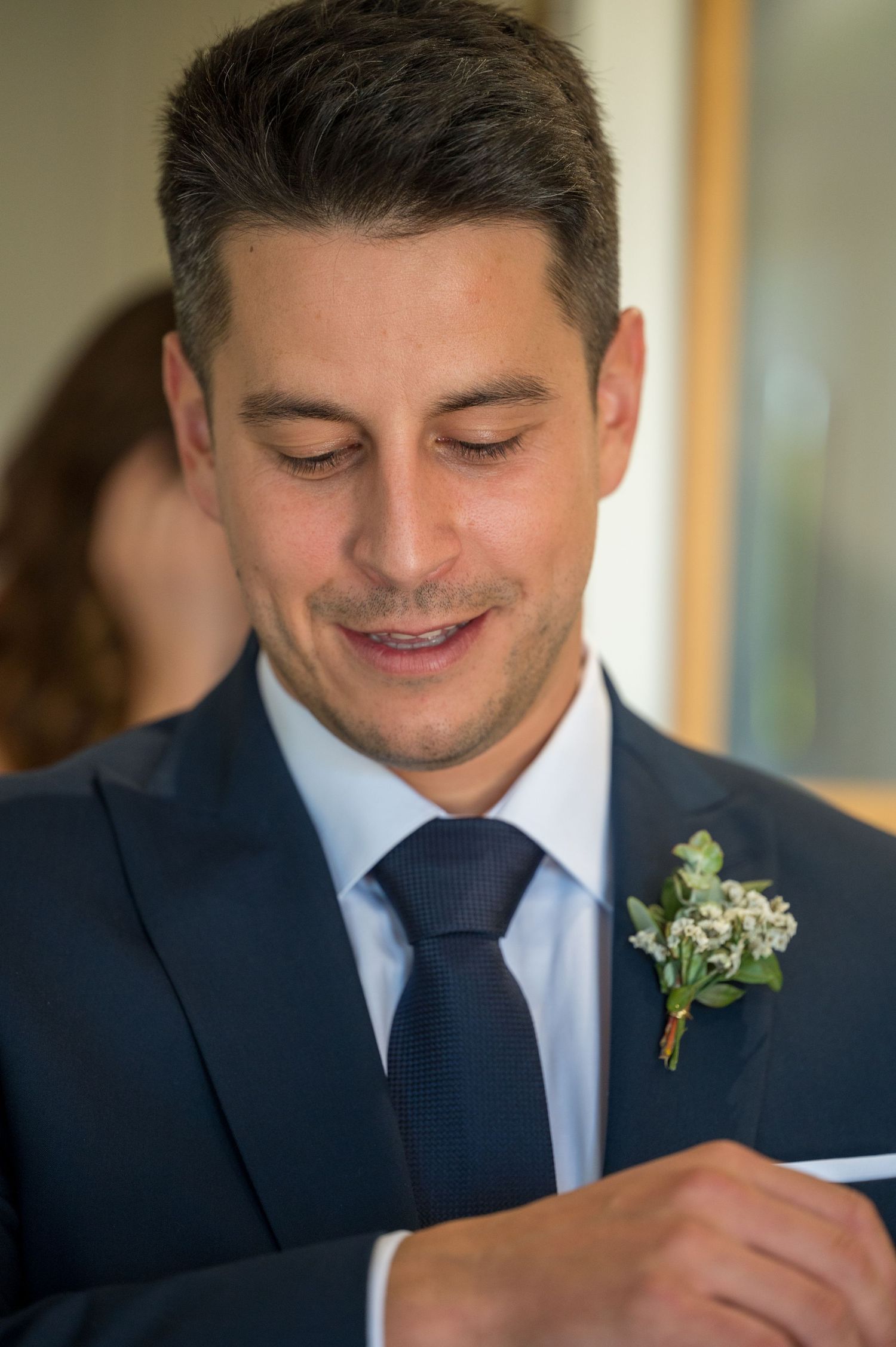 A groom in a navy suit with floral boutonniere looks down while writing.