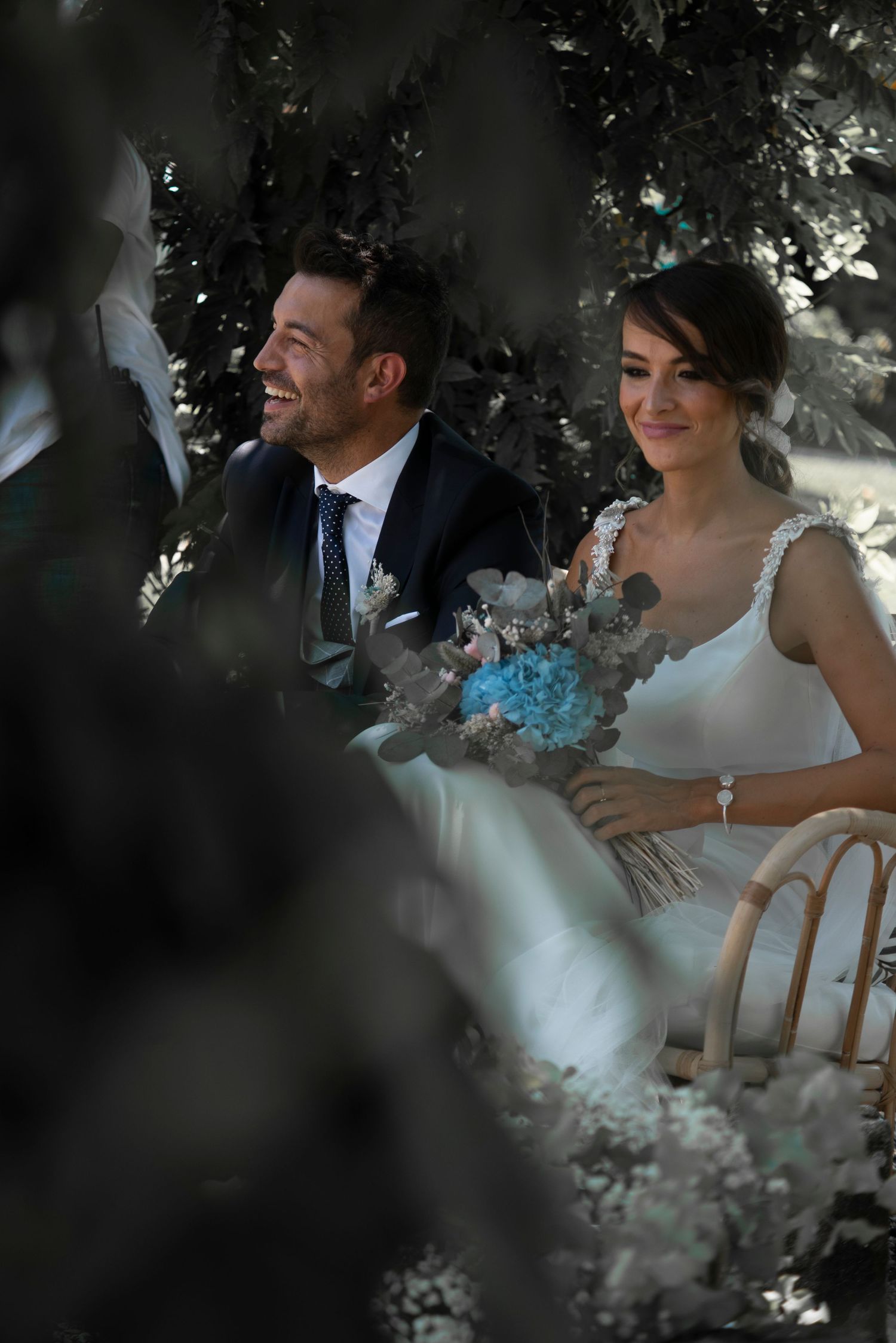 A happy couple at their wedding ceremony, with the bride holding a blue and white bouquet.