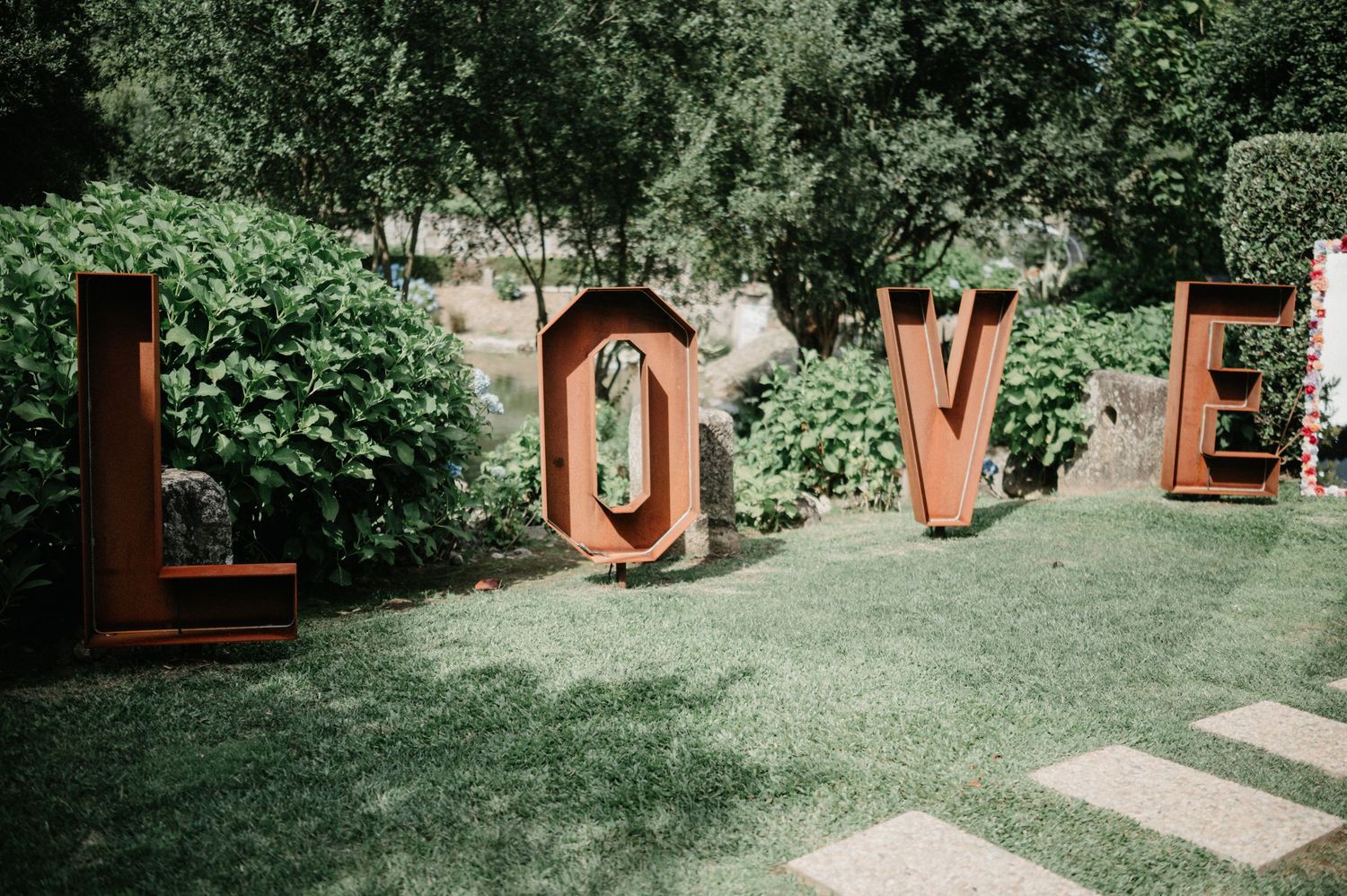 A lush garden wedding venue with wooden structures and green landscaping on a sunny day.