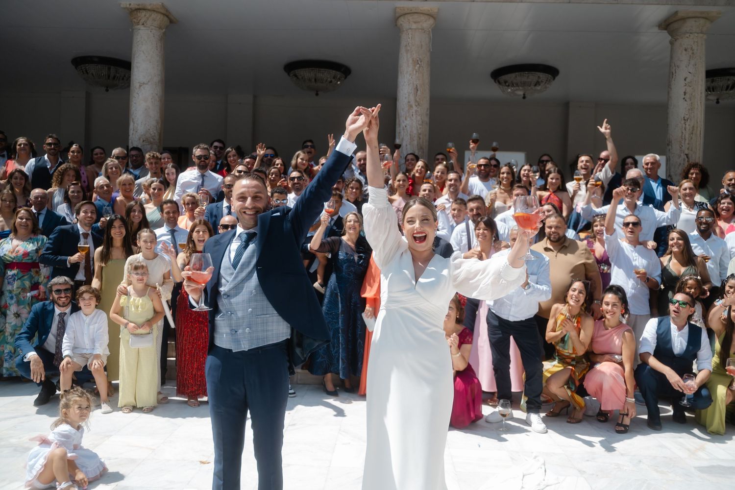 Wedding guests dance together on a crowded dance floor at an indoor reception venue.