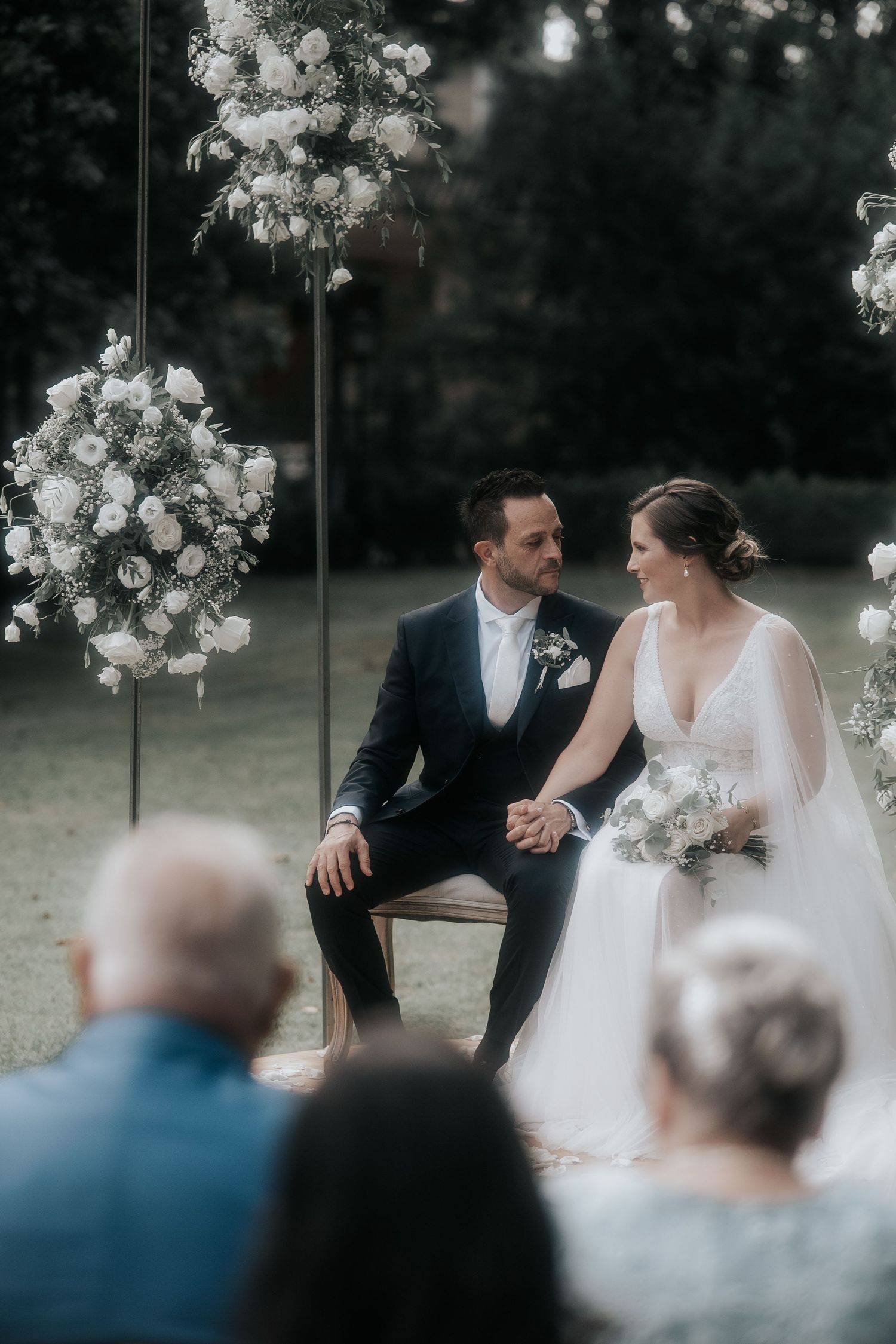 Intimate outdoor wedding ceremony with floral arrangements and guests seated in background.