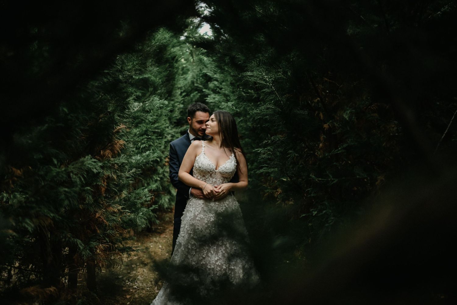 A couple embraces in a romantic outdoor photoshoot surrounded by lush green forest scenery.