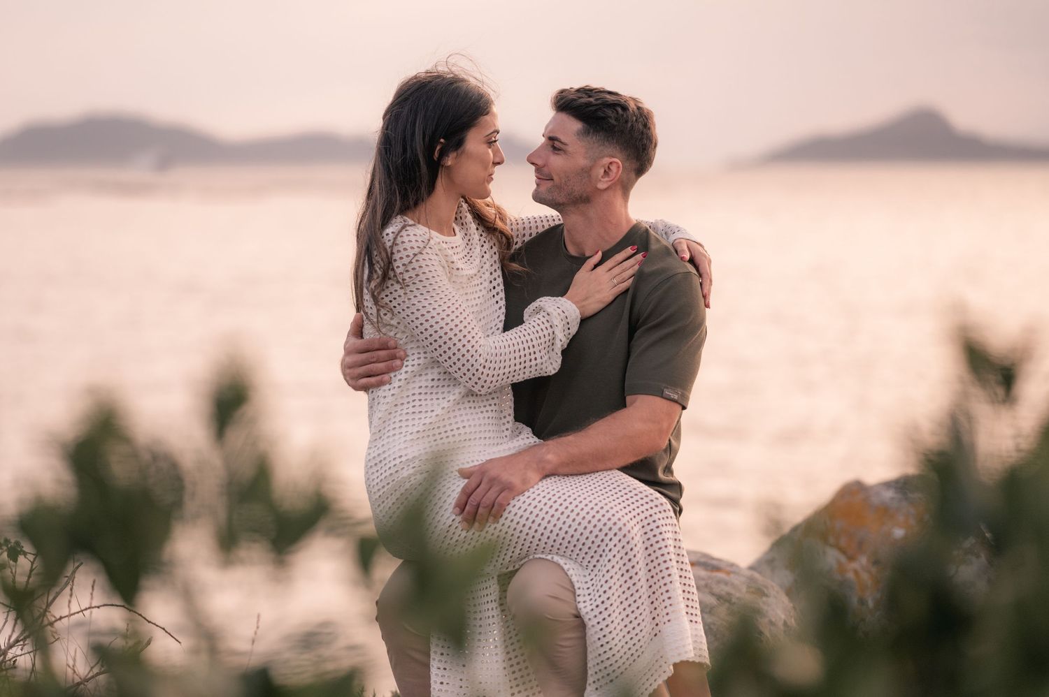 Loving couple shares romantic moments at sunset with mountains and ocean in the background.