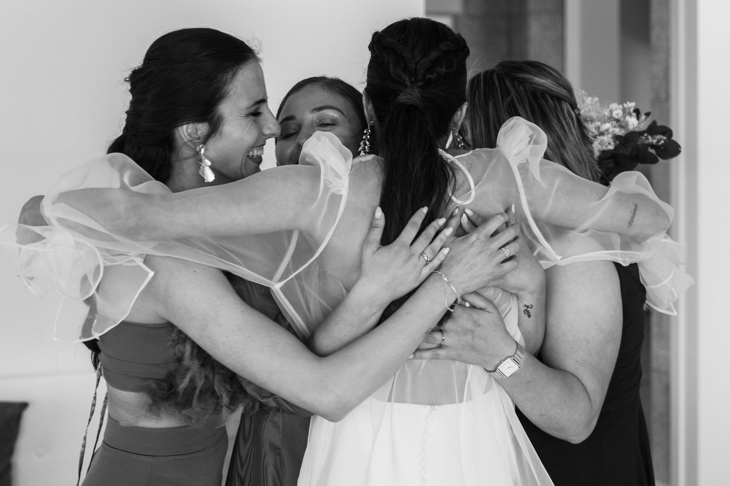 A group of bridesmaids share an intimate emotional embrace in a black and white candid wedding moment.