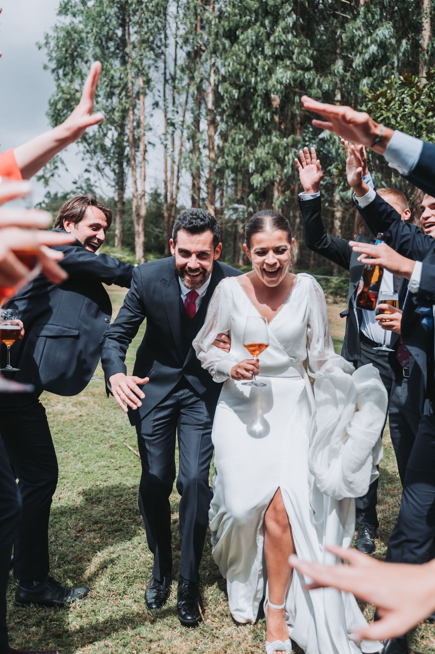 Joyful celebration at an outdoor wedding with guests raising glasses and arms in a festive toast.