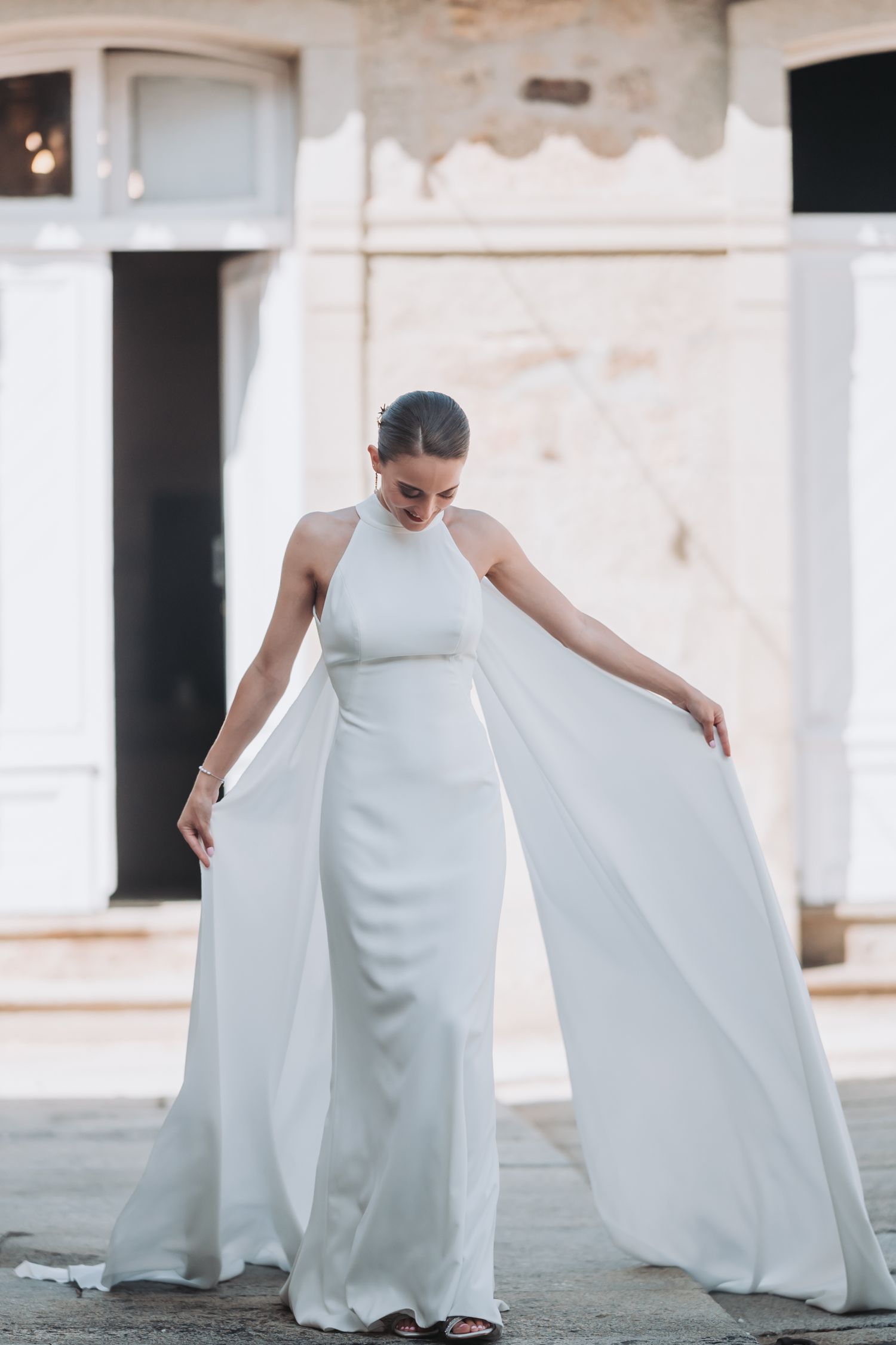 Flowing white wedding dress with train captured in movement against light interior.