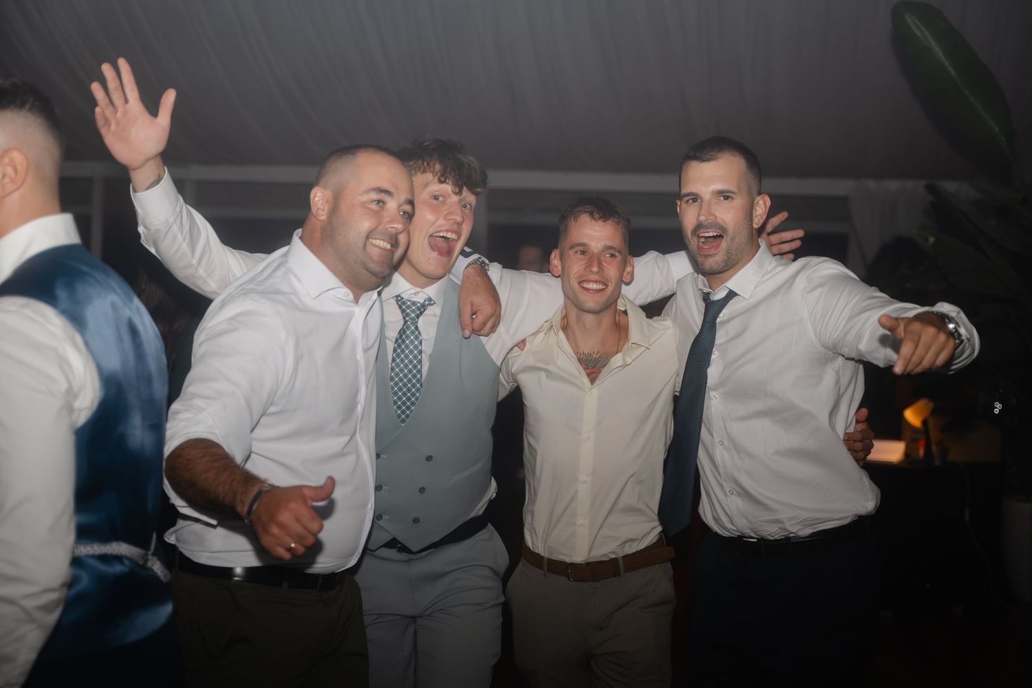 Wedding guests dance and celebrate together on a dimly lit dance floor at an evening reception.