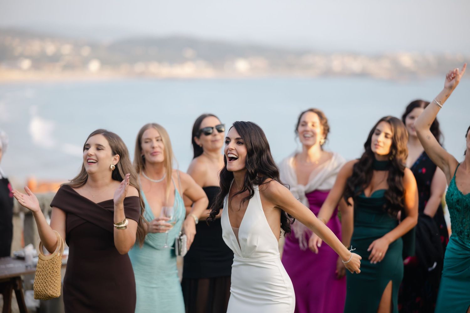 Group of friends laughing and celebrating together at sunset on the beach in casual attire.