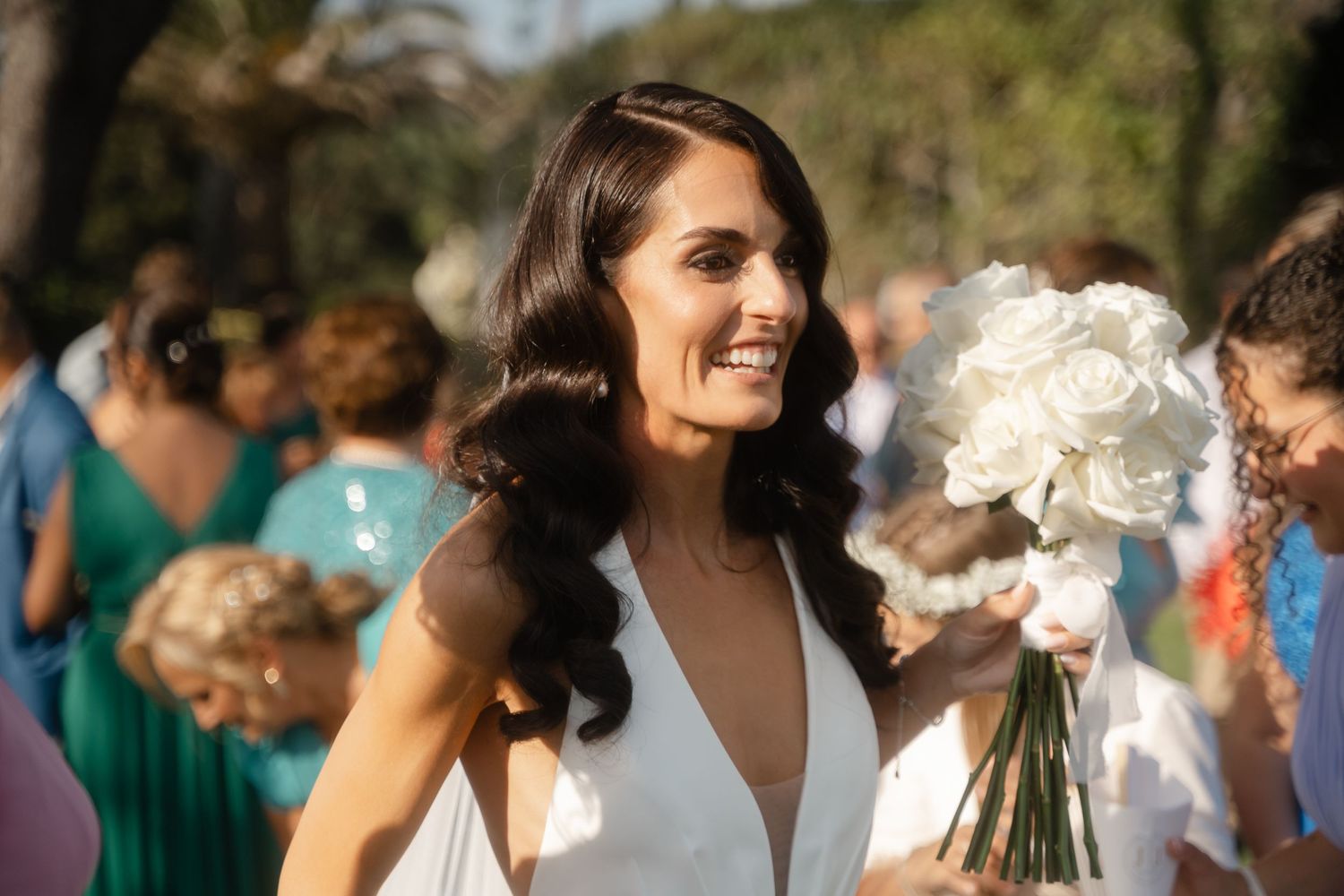 Wedding celebration outdoors with guests mingling under white floral arrangements.