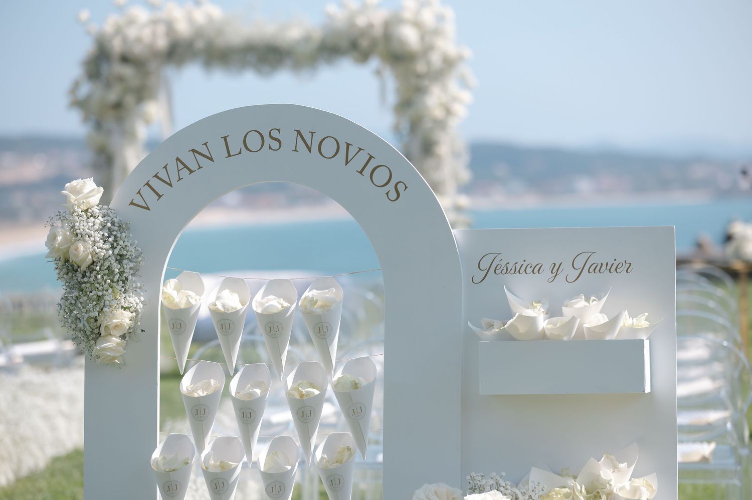 Elegant wedding reception table setup with white chairs and floral arrangements overlooking an ocean view.