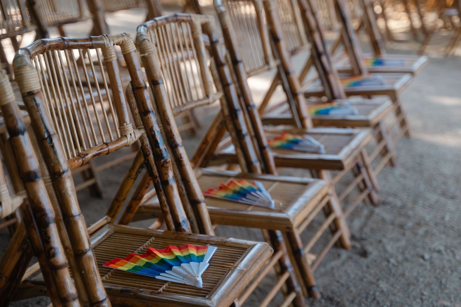 Wooden folding chairs with colorful paper fans arranged in rows for an outdoor event.