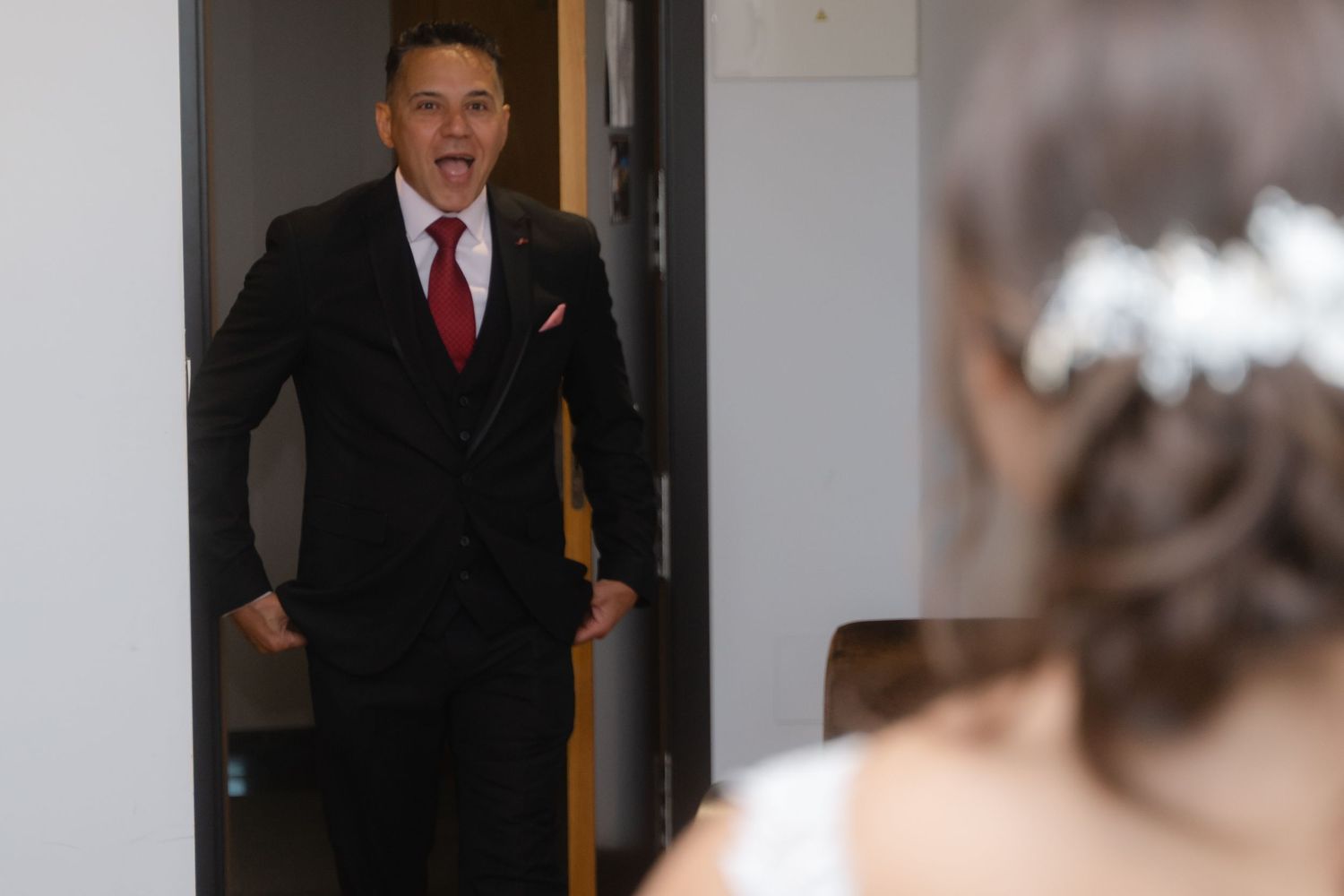A person in a black suit gestures while speaking in front of a blurred background.