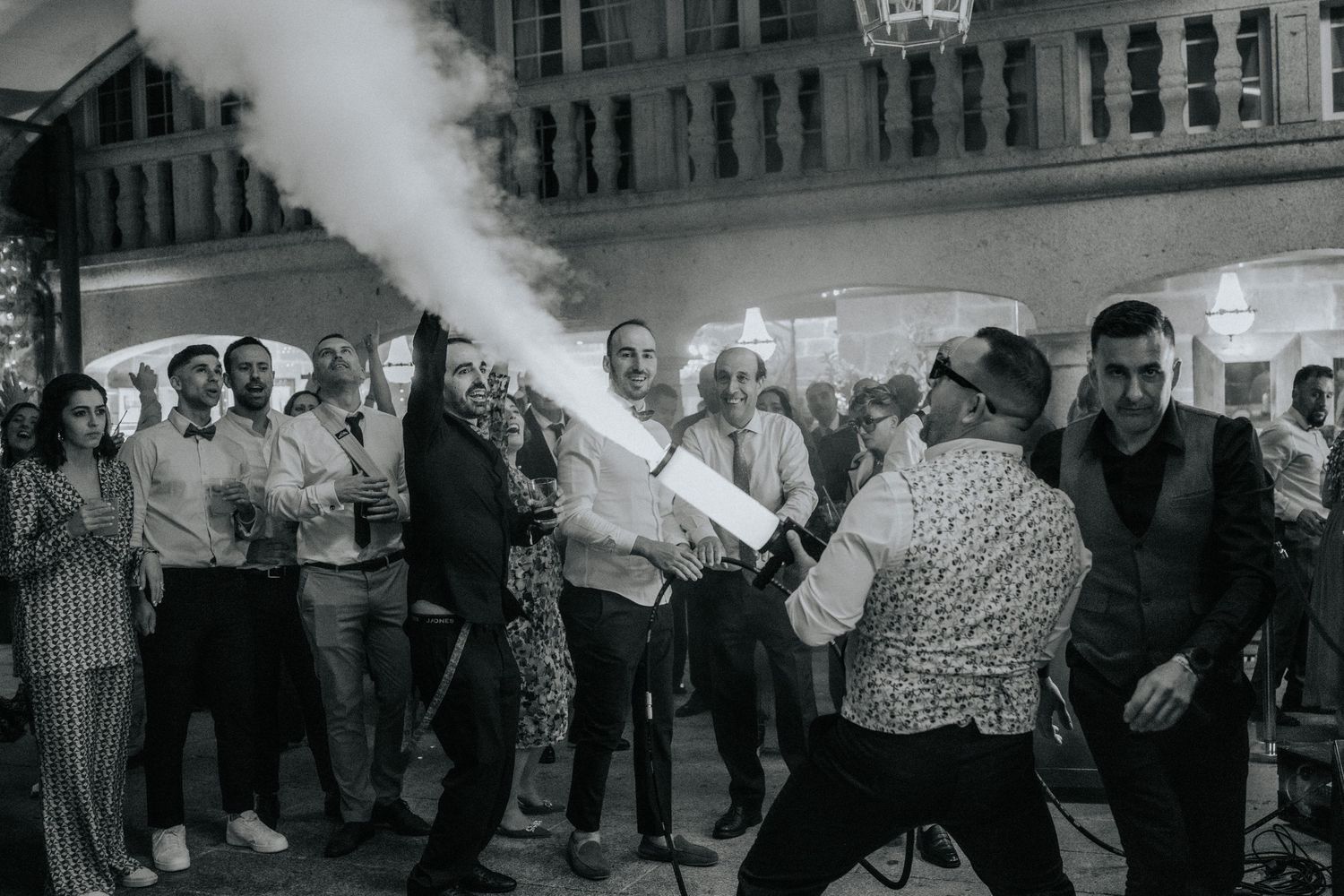 A crowd watches as someone demonstrates using a fire extinguisher on a city street in a vintage black and white photograph.