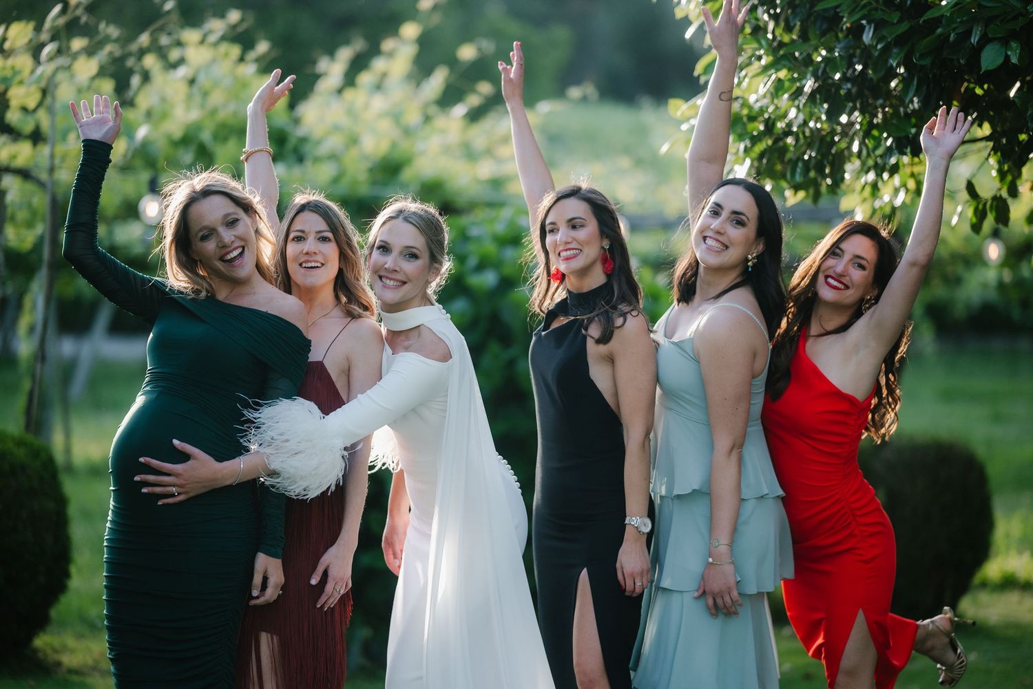 Wedding party members in formal attire pose together for photos on a sunny day in a garden.