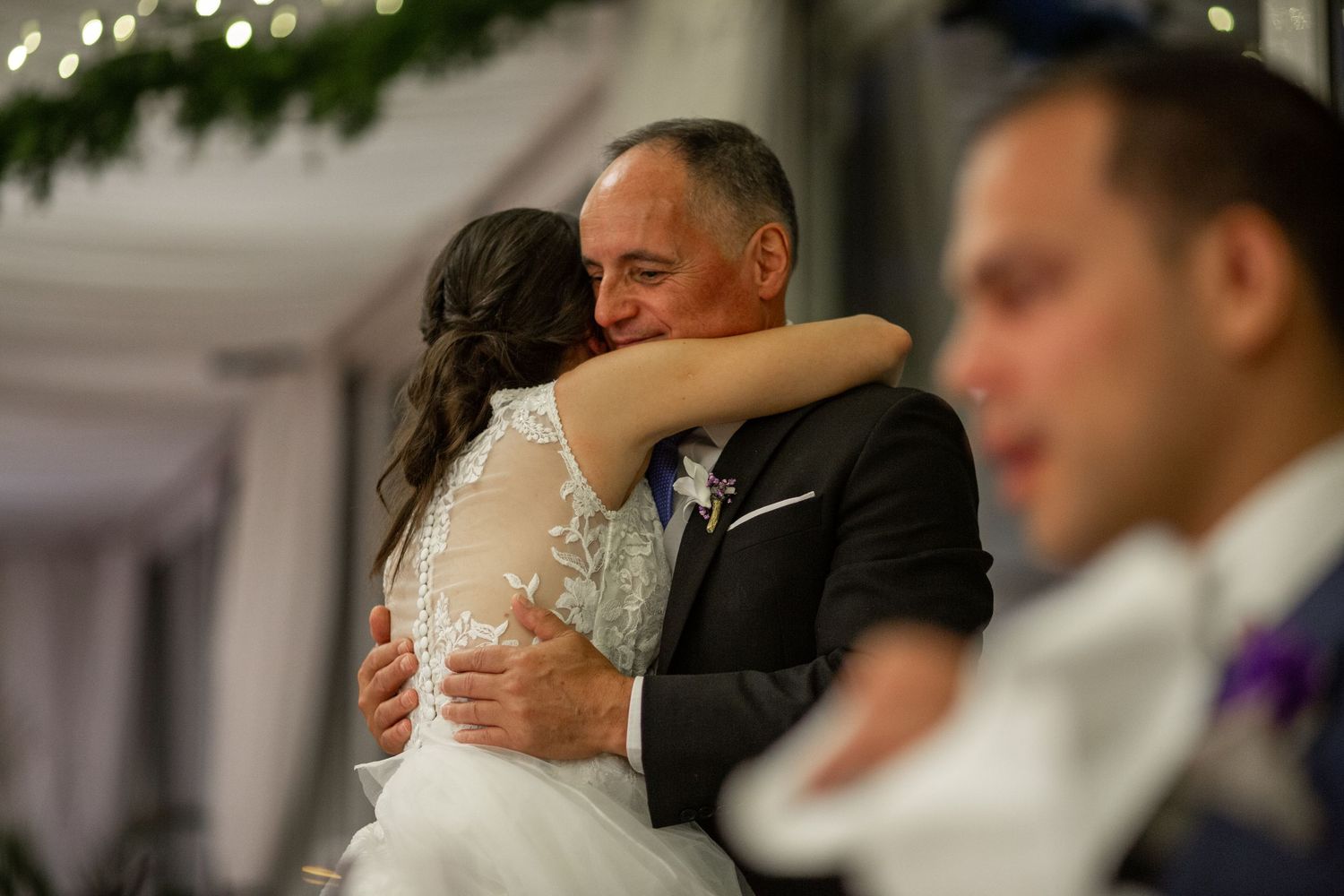Wedding guests embrace and dance together at a reception under elegant lighting and decor.