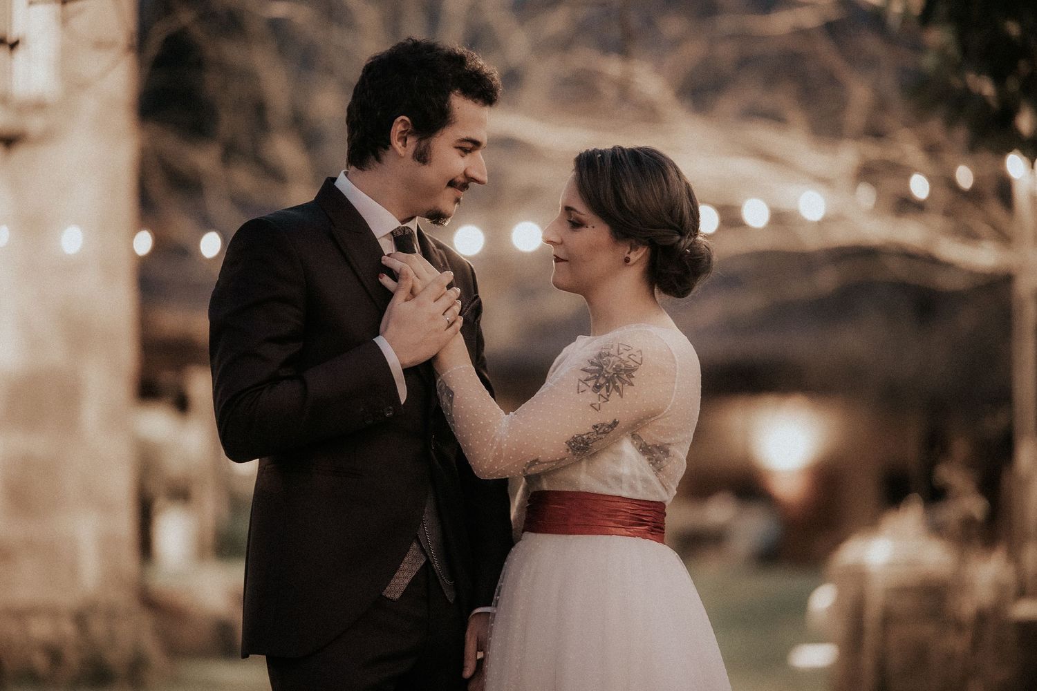 A romantic couple shares a tender moment during their wedding reception under twinkling string lights.