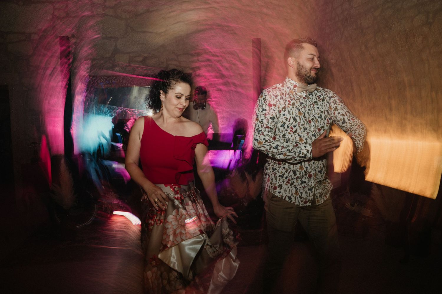 People dancing in a dimly lit room with pink and purple lighting creating a moody nightclub atmosphere.