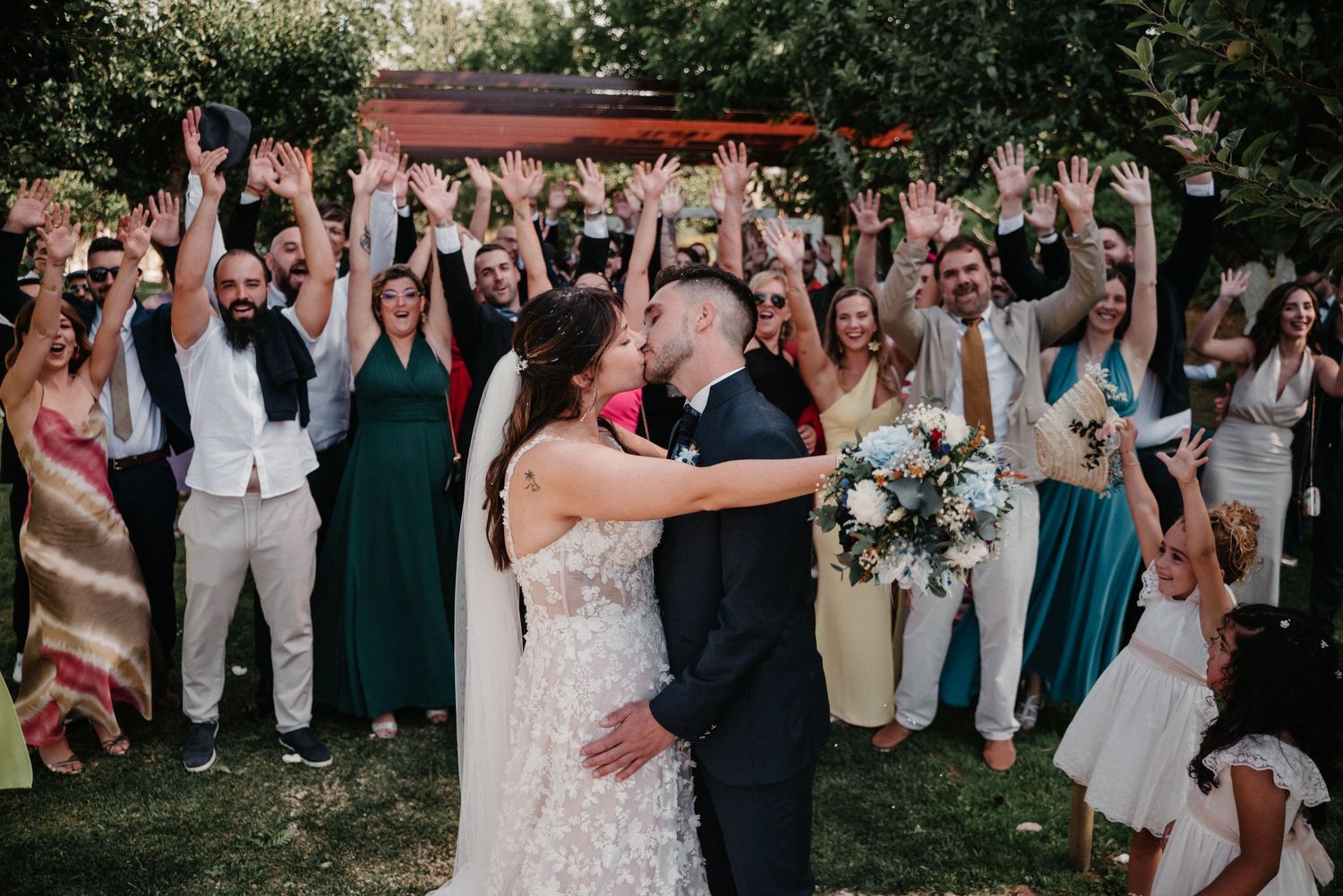 Wedding celebration with guests gathered outdoors under natural greenery and decor.