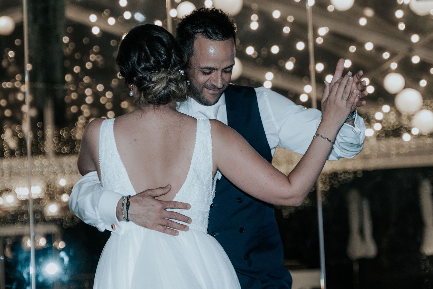 A couple shares a romantic dance together under twinkling lights at their wedding reception.