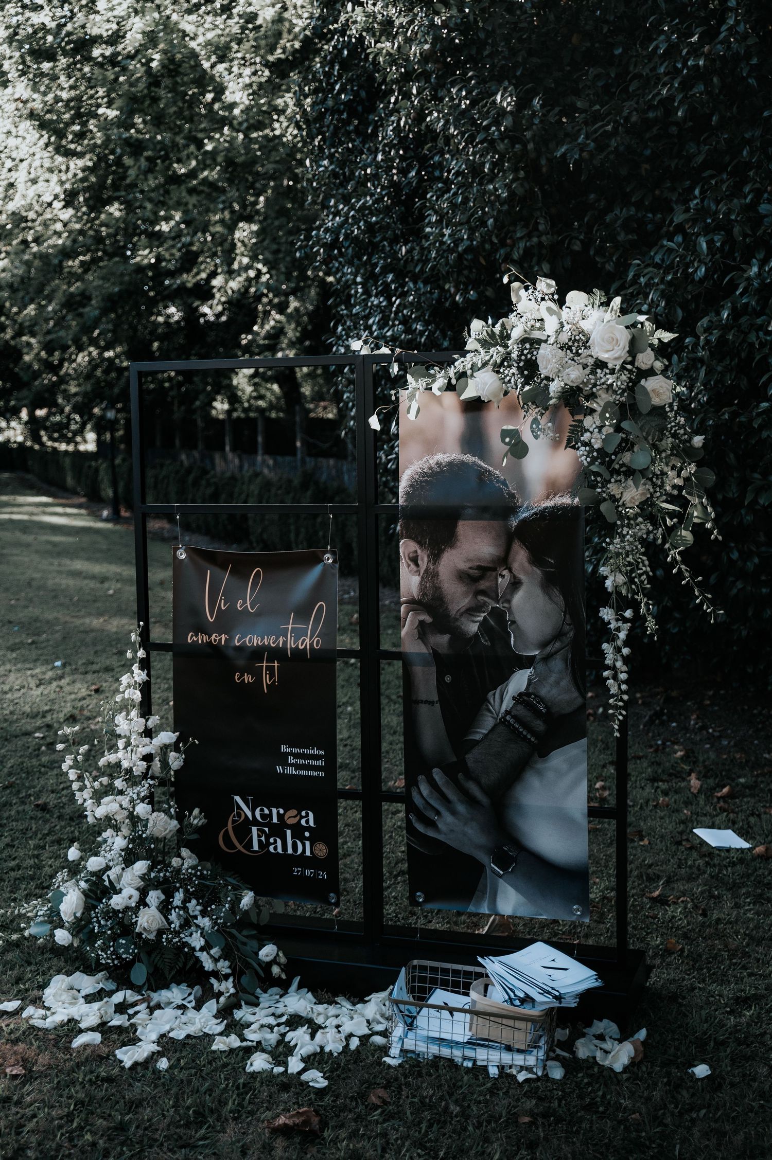 Wedding decor setup featuring black signage and floral arrangements against a dark outdoor background.