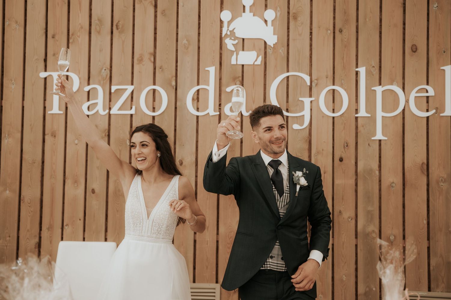 A wedding party stands in front of a rustic wooden wall during an elegant celebration.