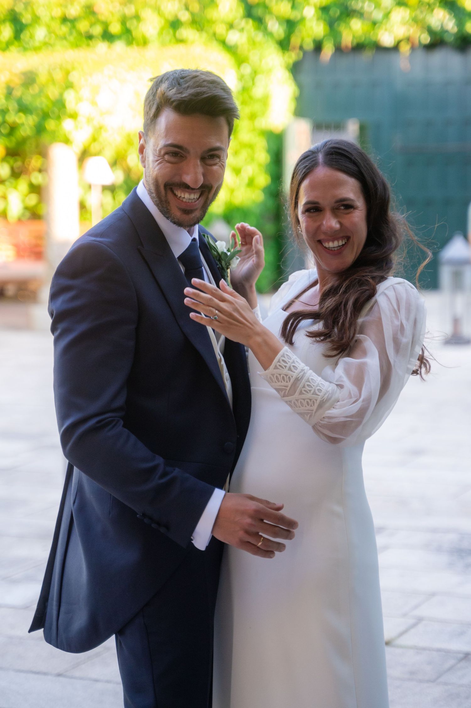 Newlyweds laugh together in a candid moment on their wedding day, surrounded by natural light and garden scenery.