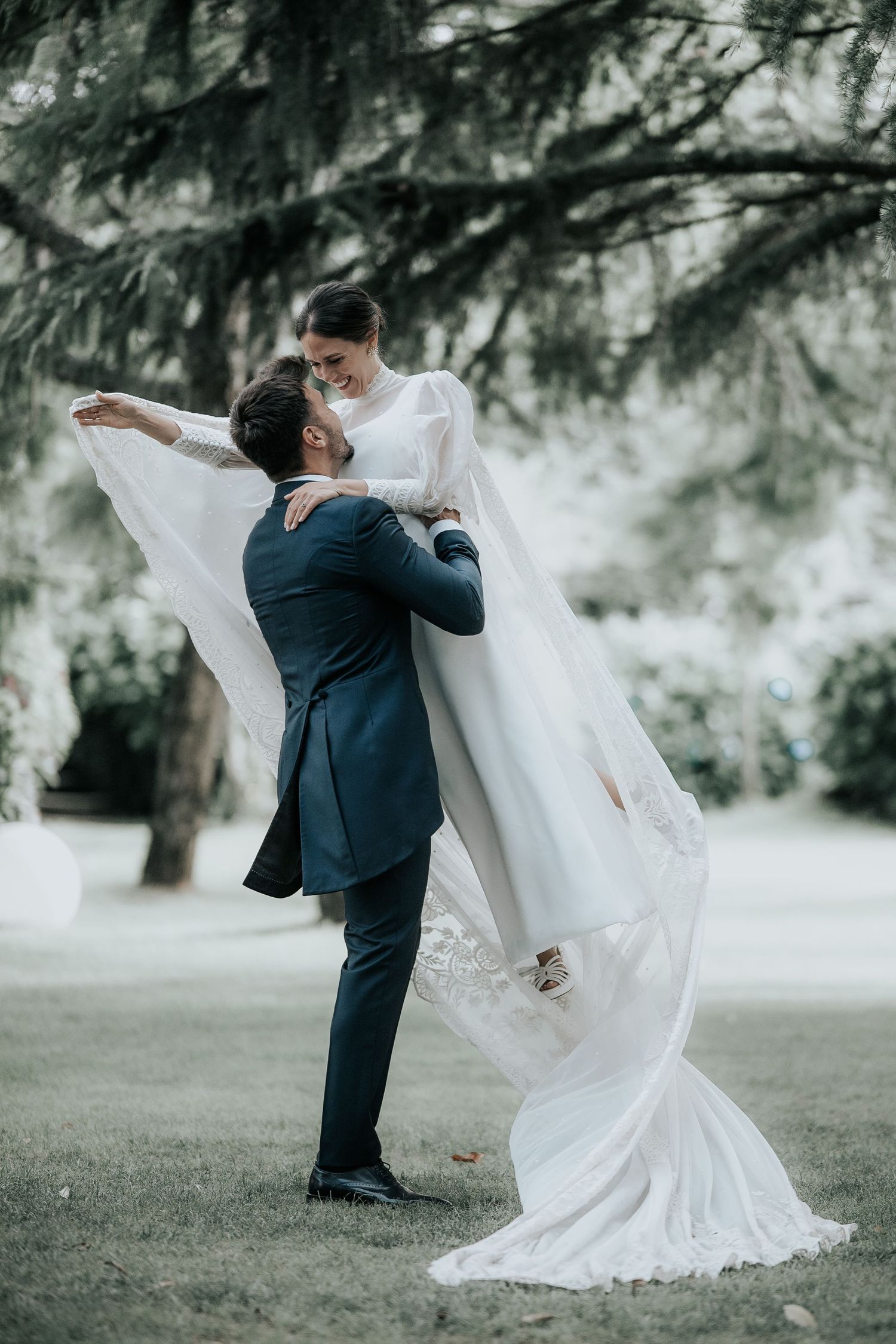 A flowing white wedding dress billows dramatically in the wind against an ethereal outdoor setting.
