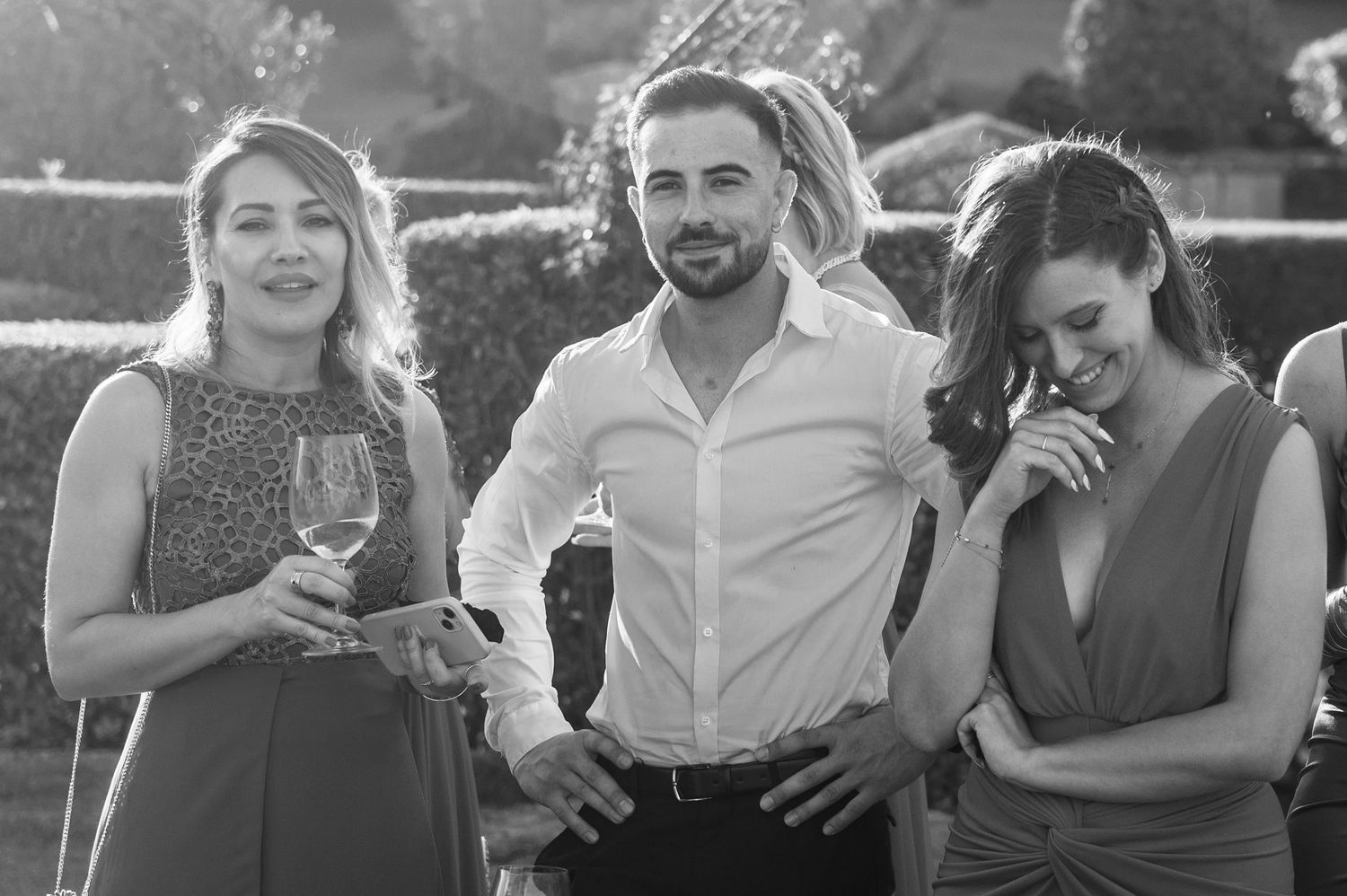 Three friends share drinks and laughter at an outdoor gathering in black and white photography.