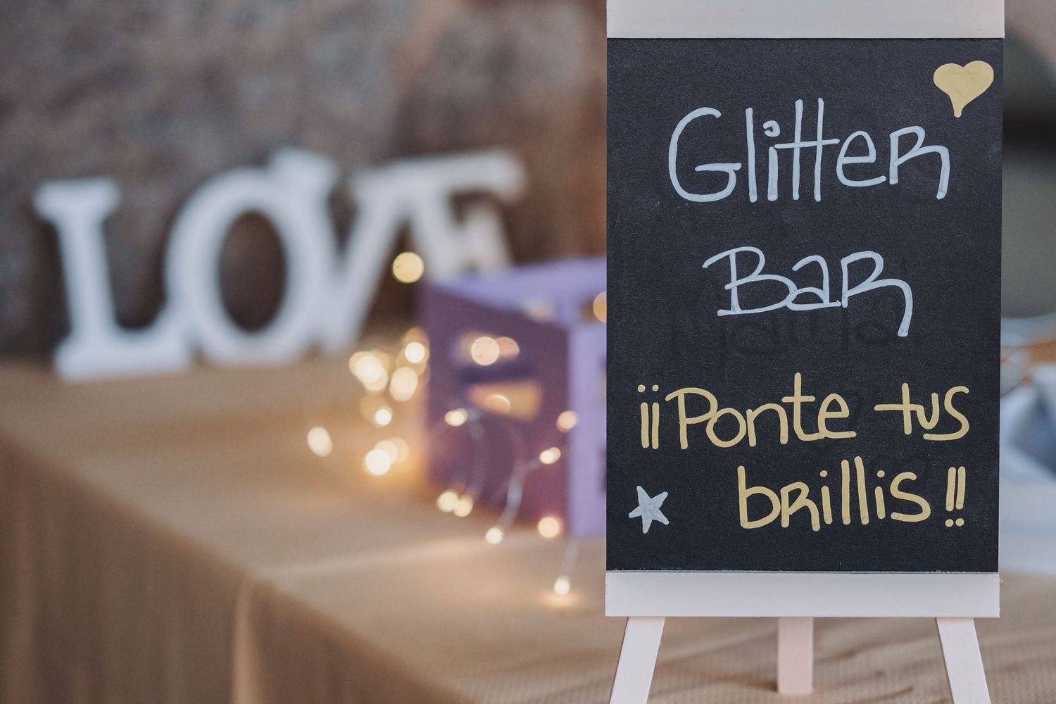 A row of decorative chalkboard signs with glittery text displays menu items and event details at a party or celebration.