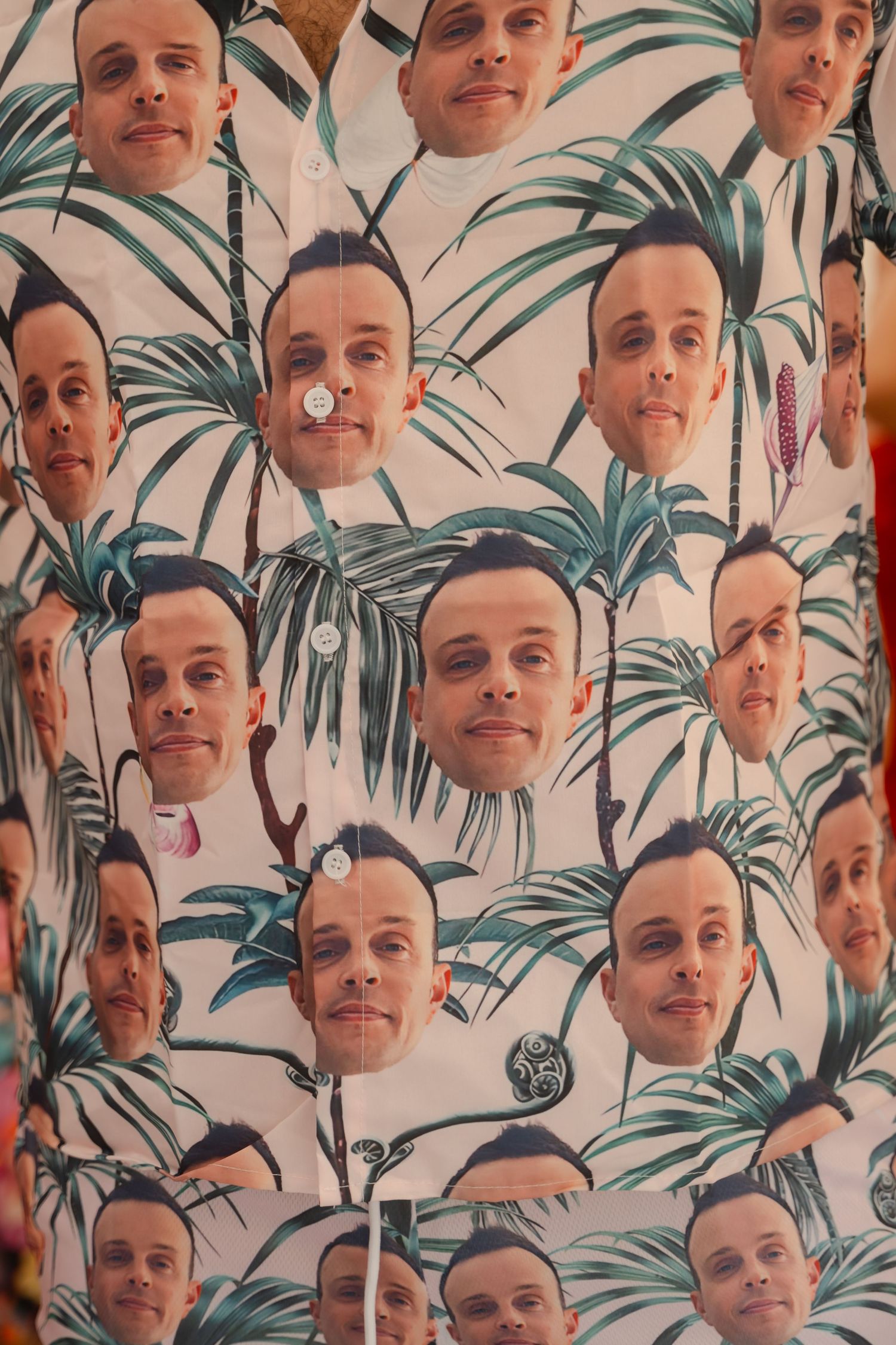 A repeating pattern wallpaper design featuring headshots arranged in rows against a tropical palm leaf background.