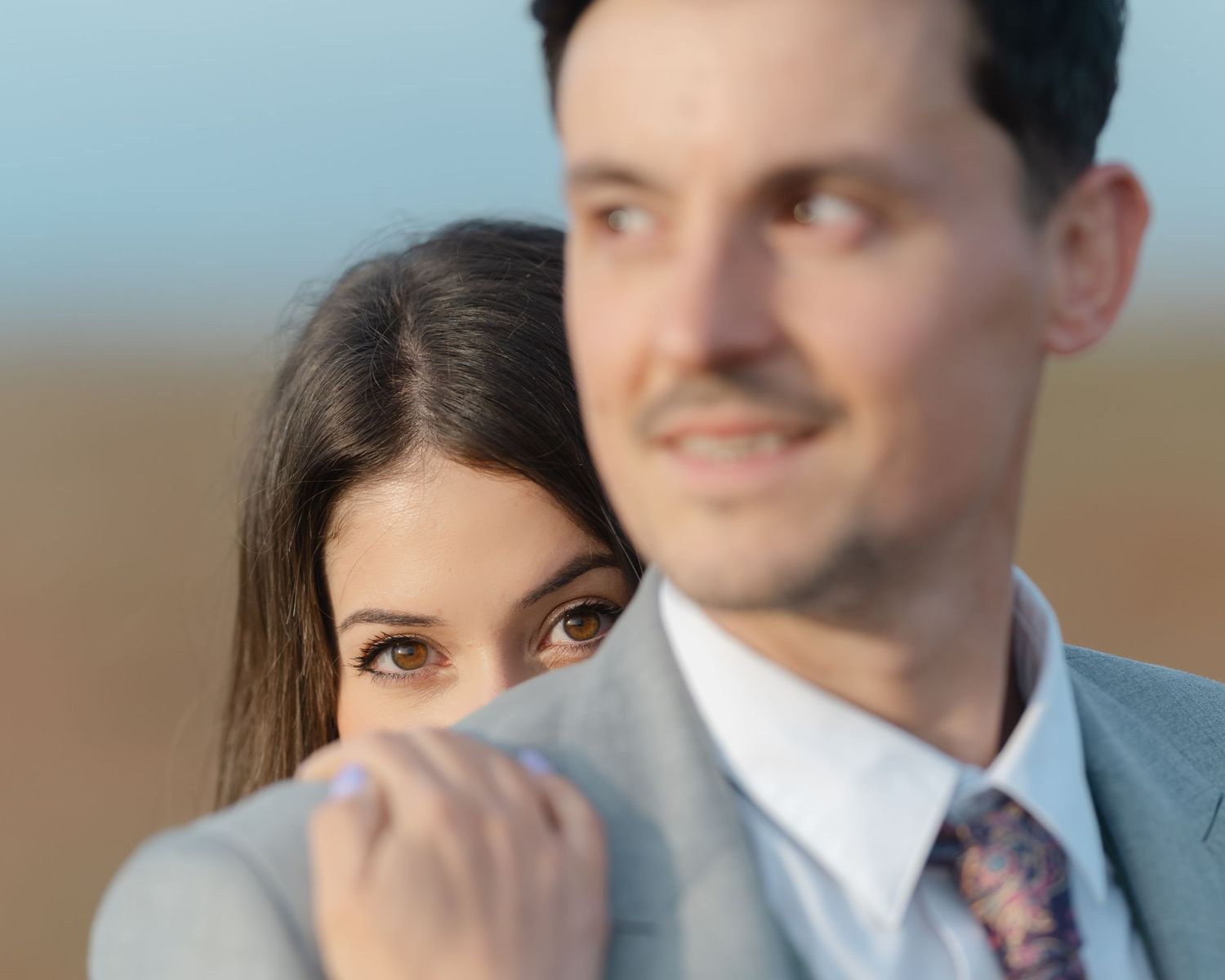 A couple in elegant attire share a romantic close-up moment outdoors with a soft blurred background.