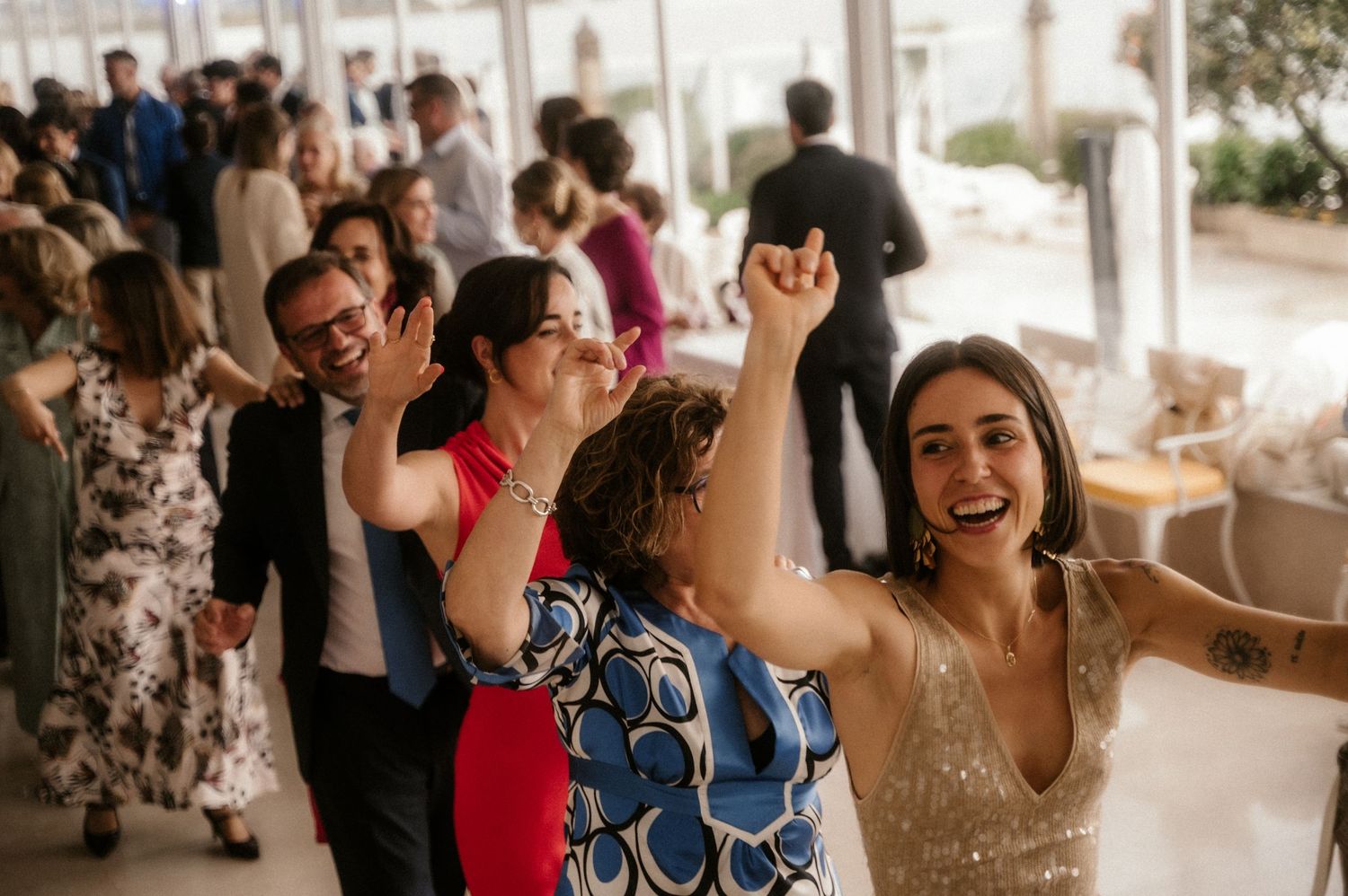 Wedding guests dance and celebrate joyfully on a crowded dance floor at an indoor reception.