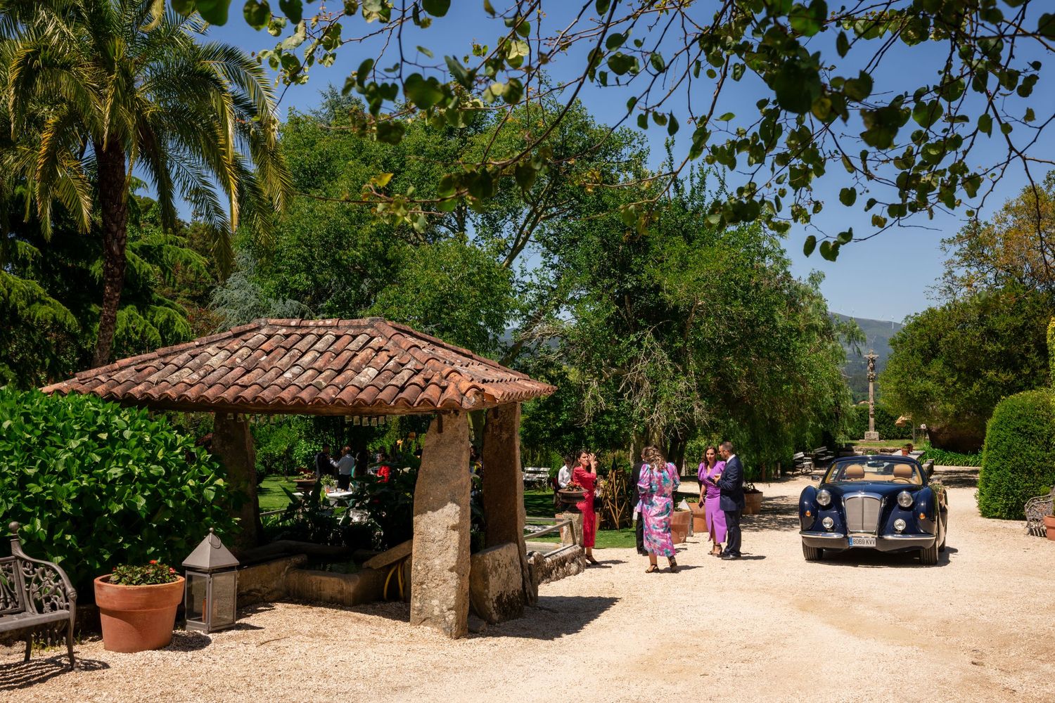 A panoramic view of a lush garden setting with stone pathways and Mediterranean architecture under blue skies.