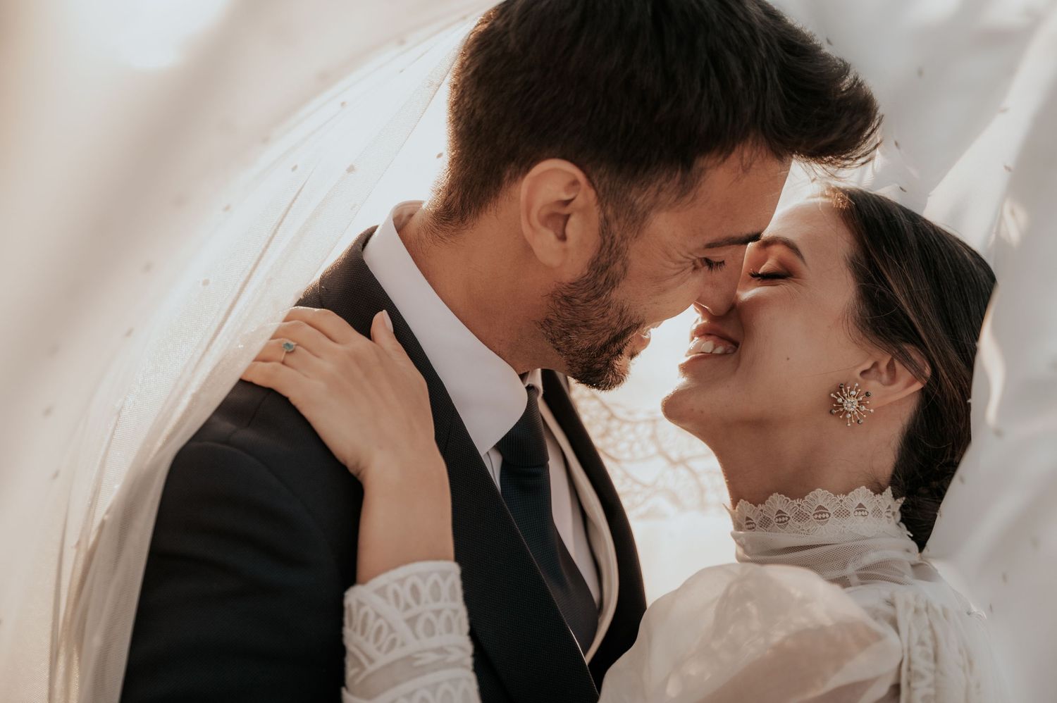 Intimate wedding portrait showing tender moment between newlyweds against white backdrop.