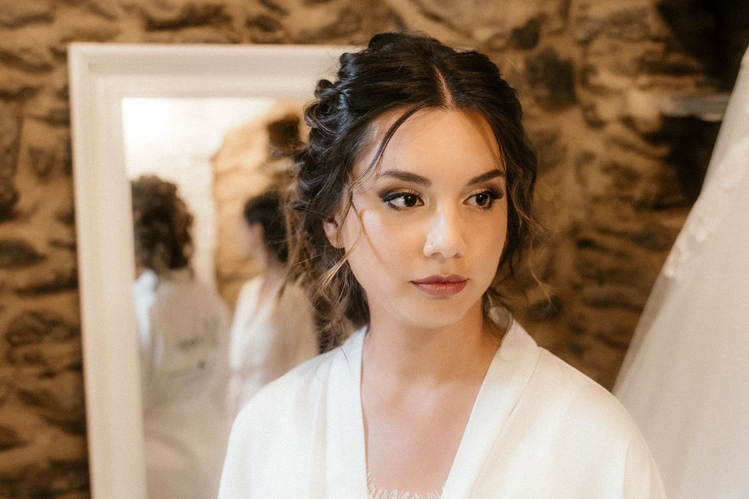 Person wearing white silk robe with elegant updo hairstyle in rustic stone room setting.